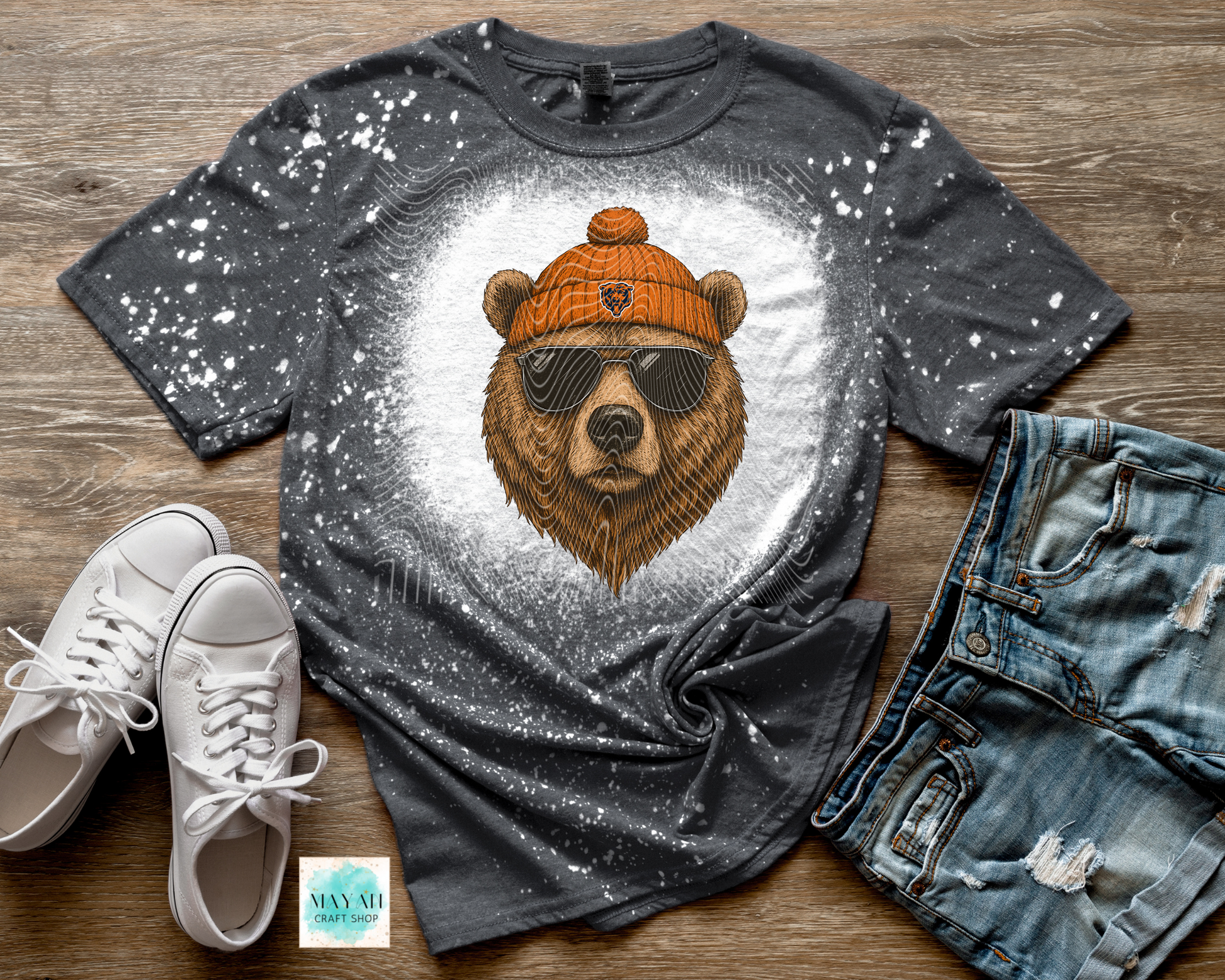 Gray t-shirt with bear graphic, sunglasses, and orange beanie on a wooden surface with white sneakers and jeans.