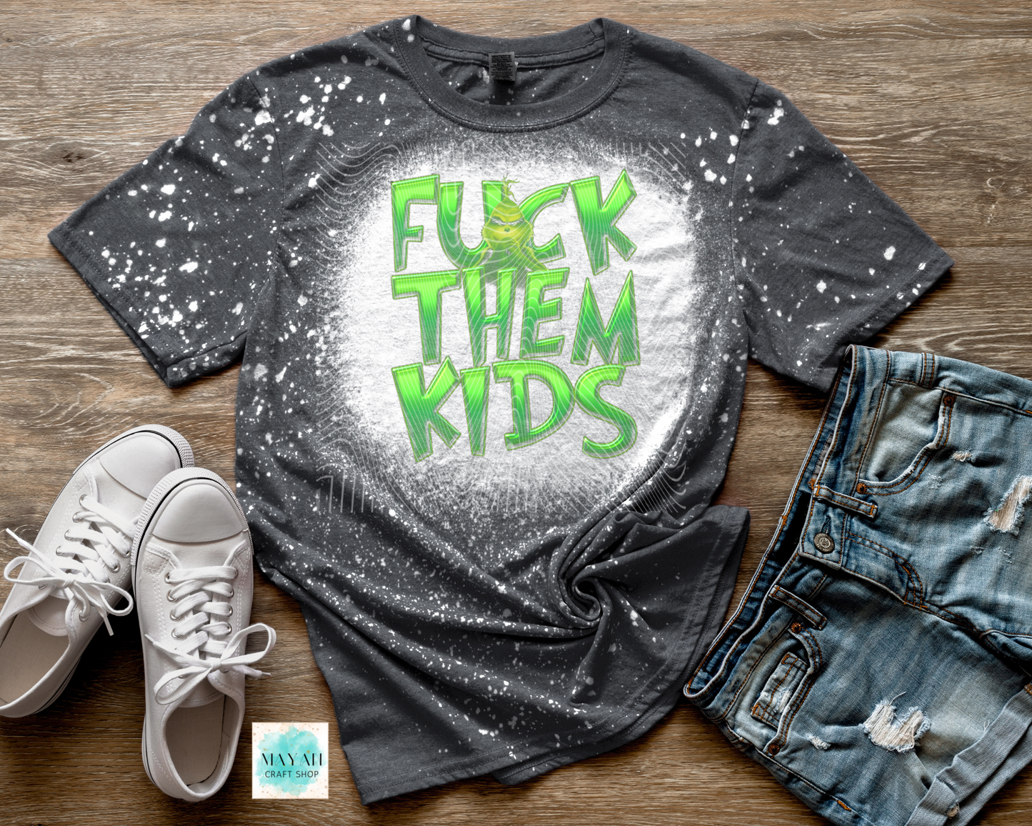 Gray t-shirt with green text, white sneakers, and jeans on a wooden surface