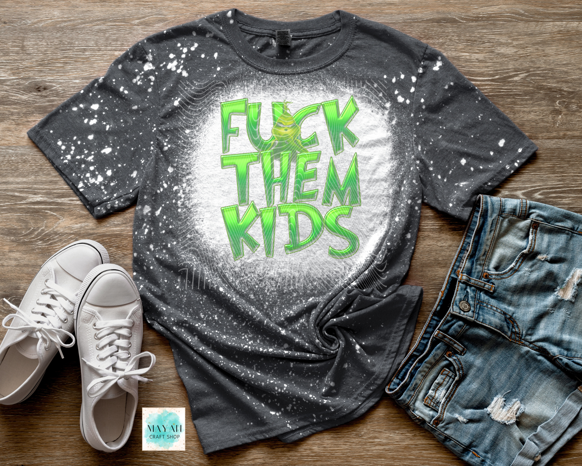 Gray t-shirt with green text, white sneakers, and jeans on a wooden surface