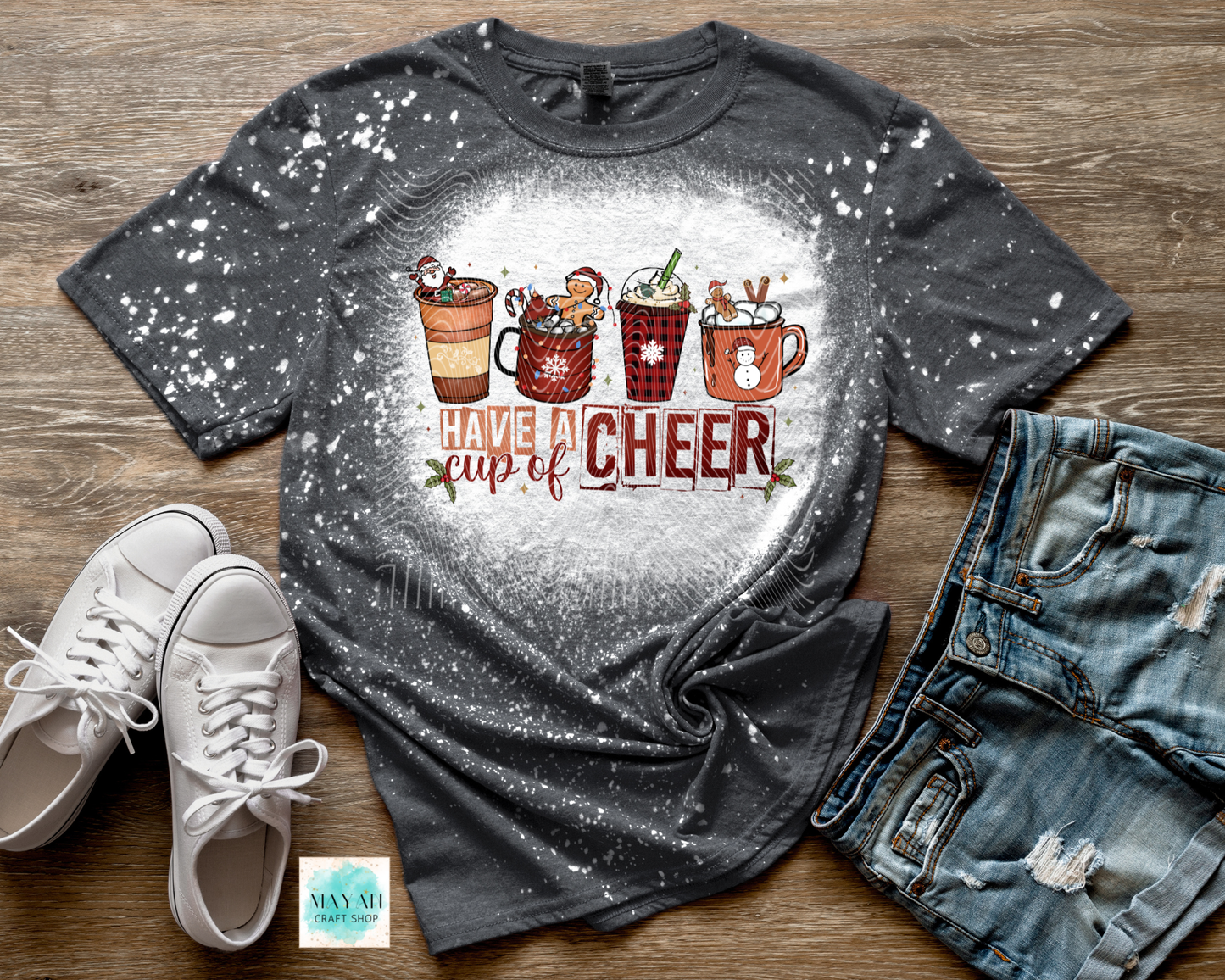 Gray t-shirt with 'Have a cup of cheer' design on a wooden surface with shoes and jeans.
