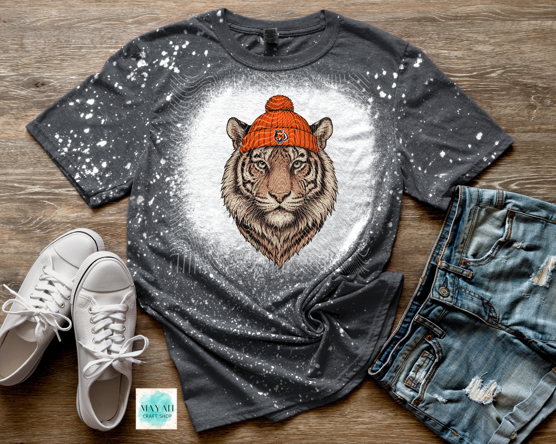 Gray t-shirt with tiger graphic wearing an orange beanie, paired with white sneakers and blue jeans on a wooden surface.