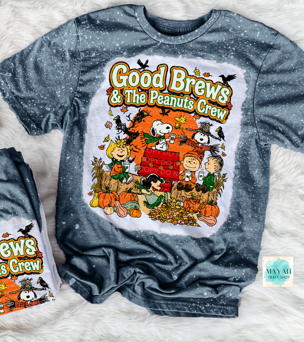 A gray heathered t-shirt featuring a large graphic print of 'Good Brews' with characters in an autumn setting. The shirt is laid flat on a white faux fur background, with a smaller folded view of the shirt visible on the left.
