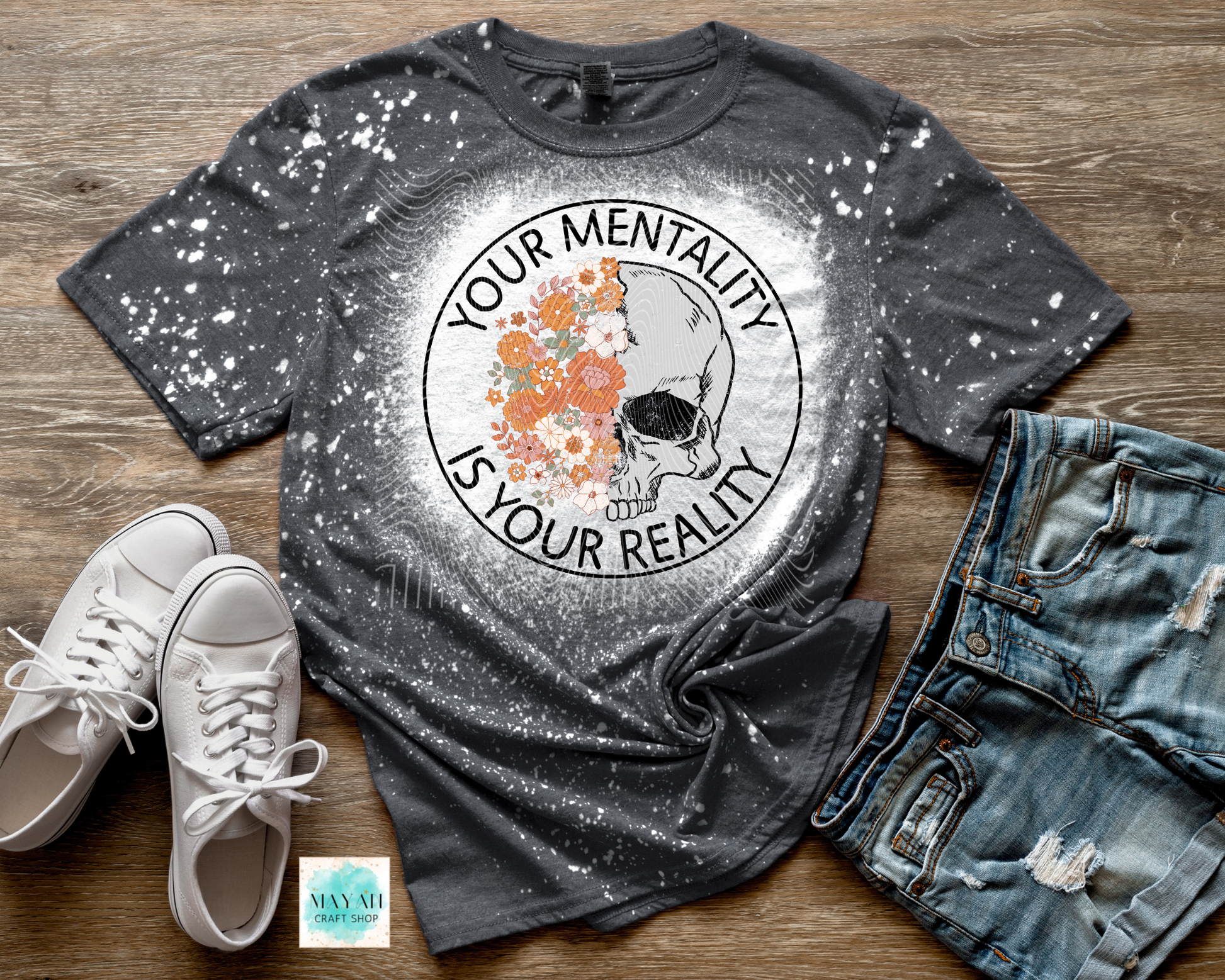 Gray t-shirt with graphic design and text on a wooden surface with shoes and jeans.
