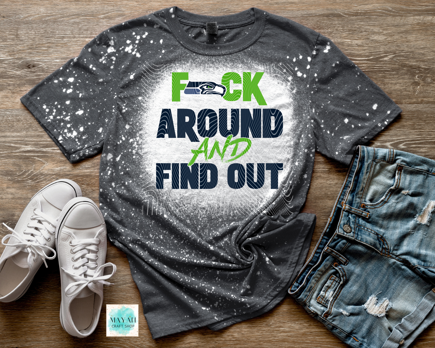 Gray t-shirt with graphic design and text on a wooden surface with shoes and jeans.