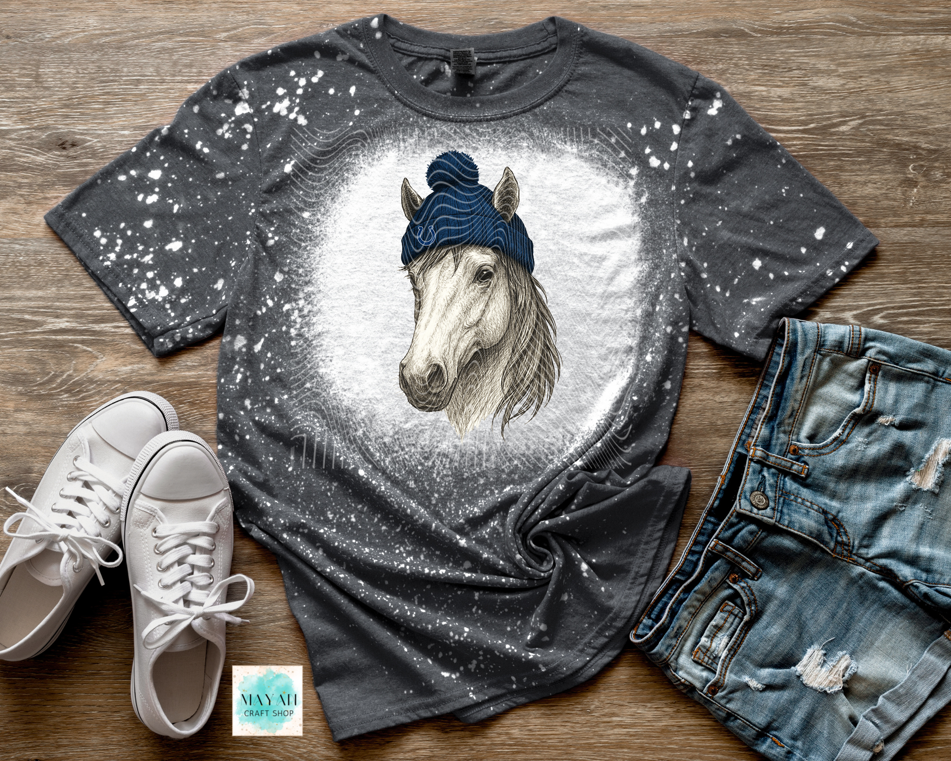 Gray t-shirt with a horse graphic, white sneakers, and denim shorts on a wooden surface.