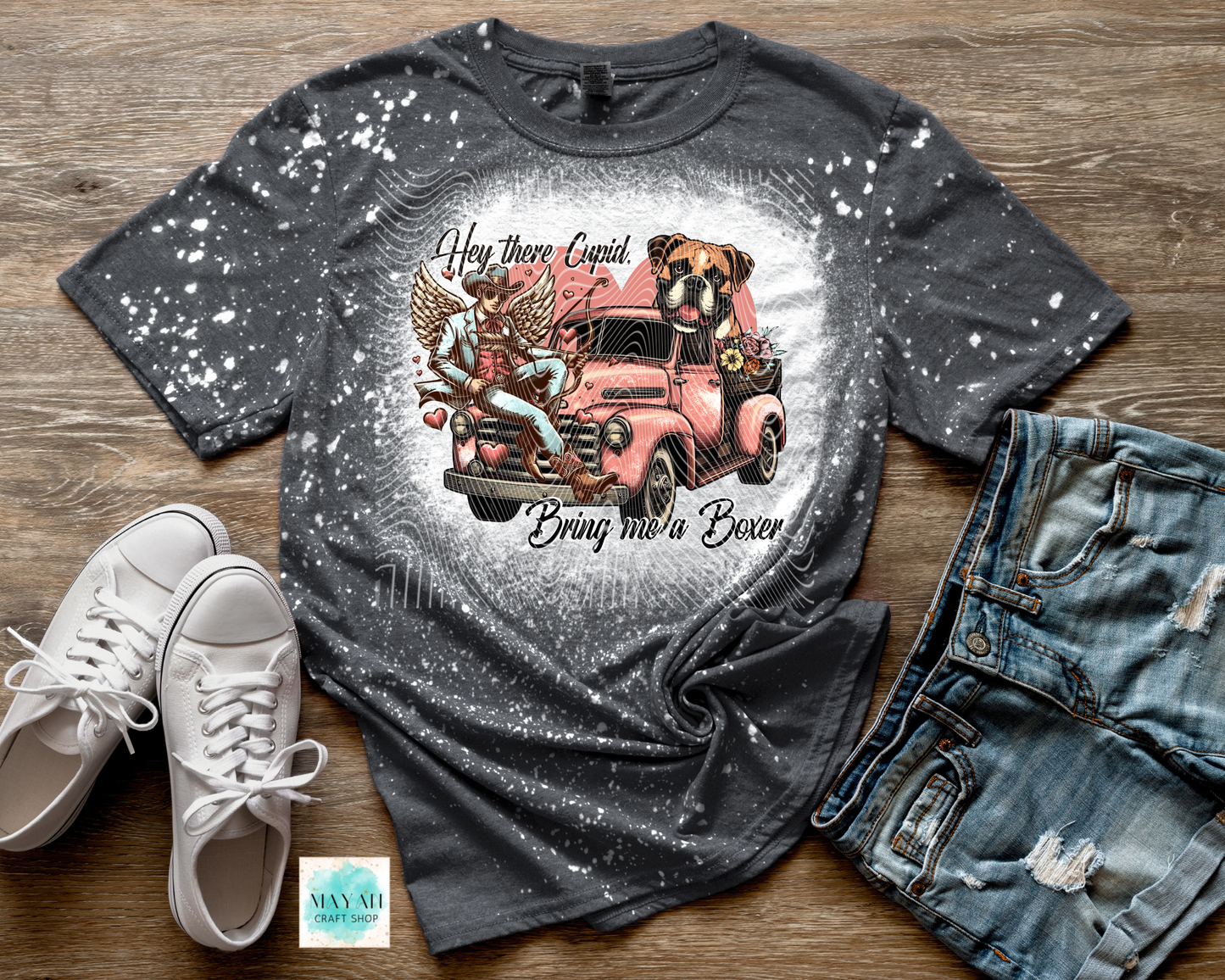 Gray t-shirt with graphic design of a pink truck and dogs, paired with white sneakers and jeans on a wooden surface.