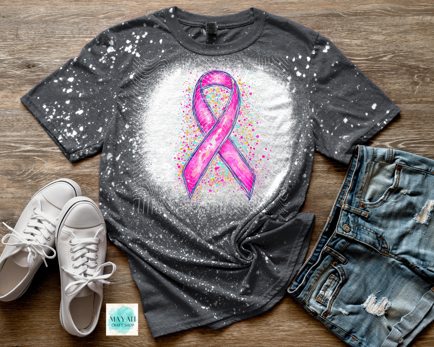 Gray t-shirt with pink ribbon design on a wooden surface with shoes and jeans.