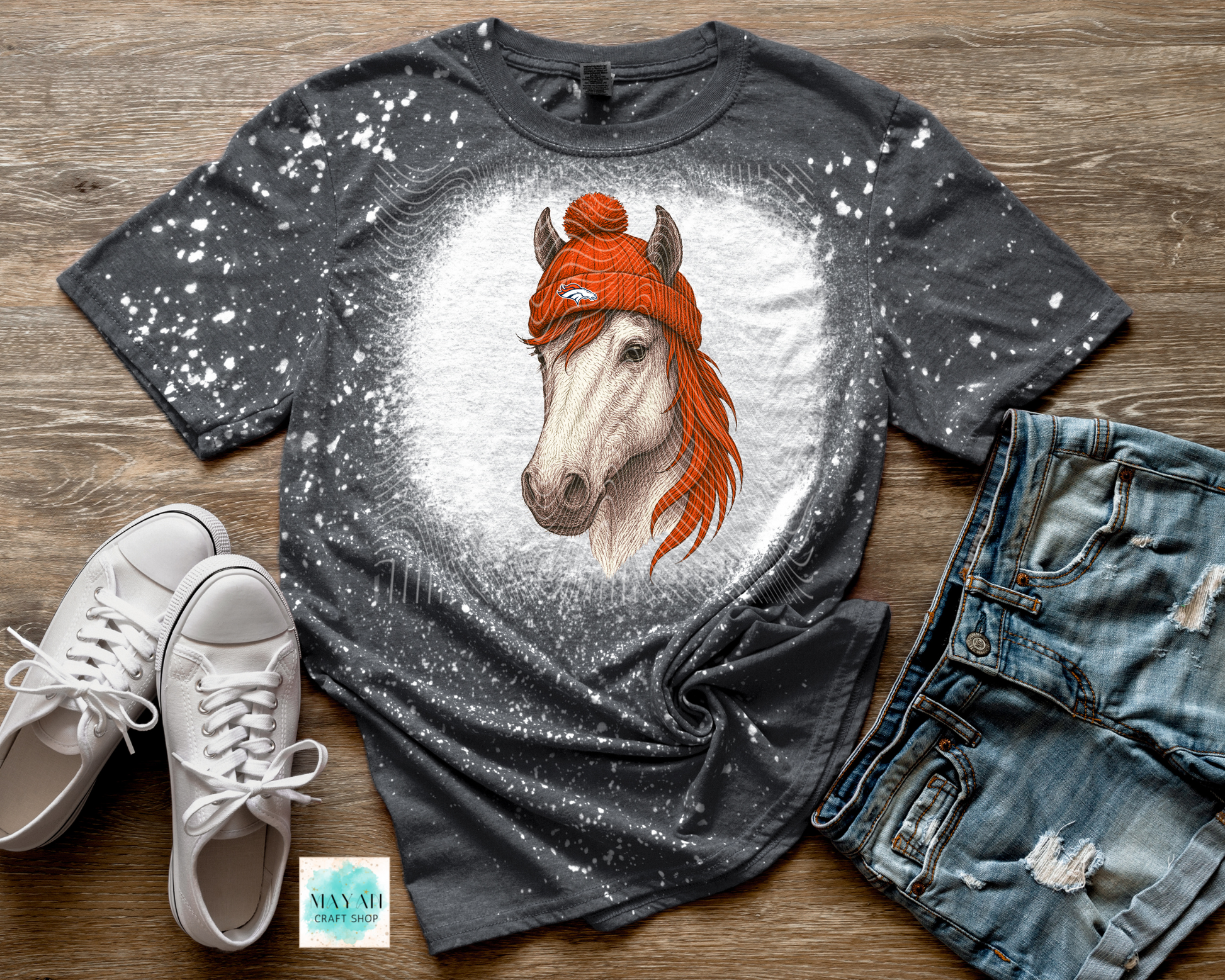 Gray t-shirt with a horse wearing an orange sweater graphic, paired with white sneakers and denim shorts on a wooden surface.