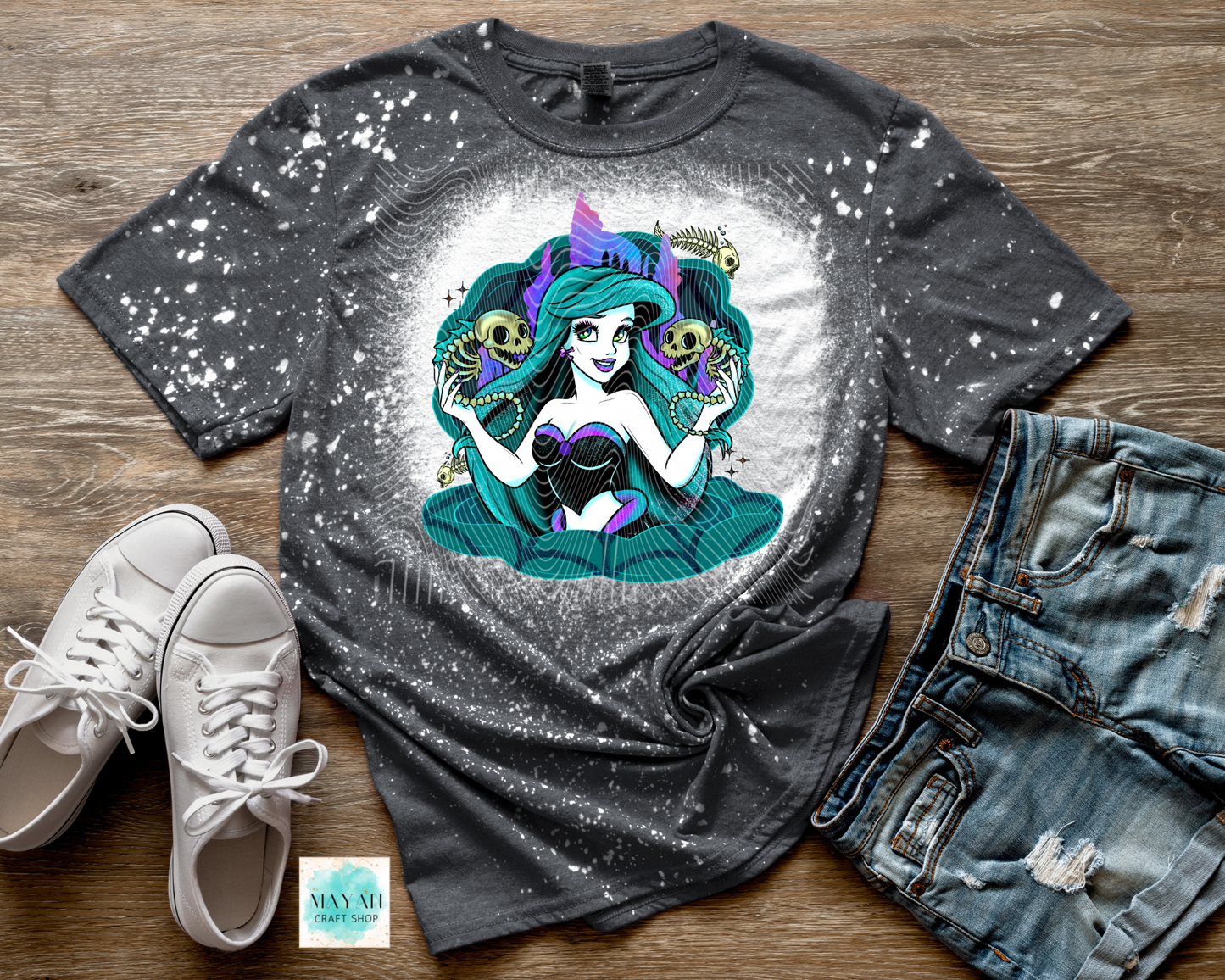 Gray t-shirt with a colorful mermaid graphic, paired with white sneakers and denim shorts on a wooden surface.