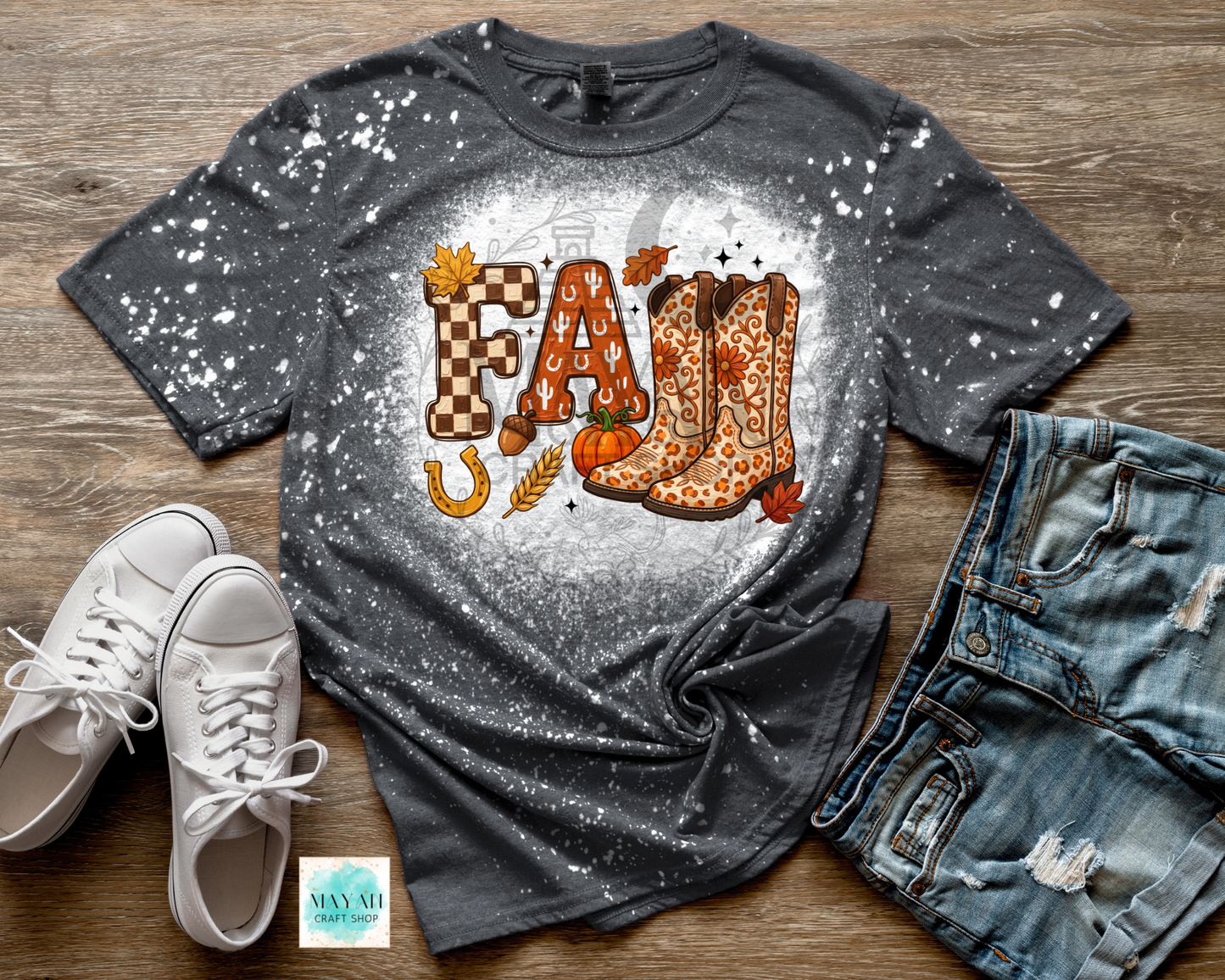 A dark gray splatter-print t-shirt featuring a 'Fall' graphic with leopard-print cowboy boots, a pumpkin, wheat, and autumn leaves, styled in a flat lay with white sneakers, distressed denim shorts.