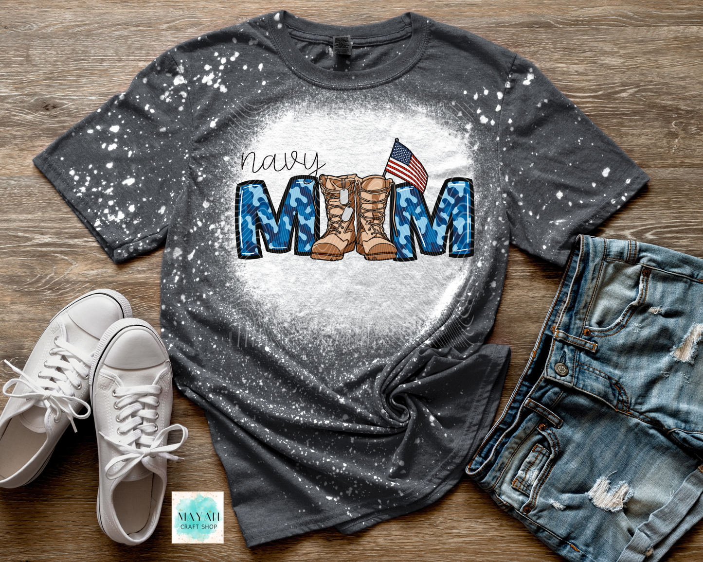Gray t-shirt with military mom design featuring boots and an American flag, displayed with white sneakers and jeans on a wooden surface.