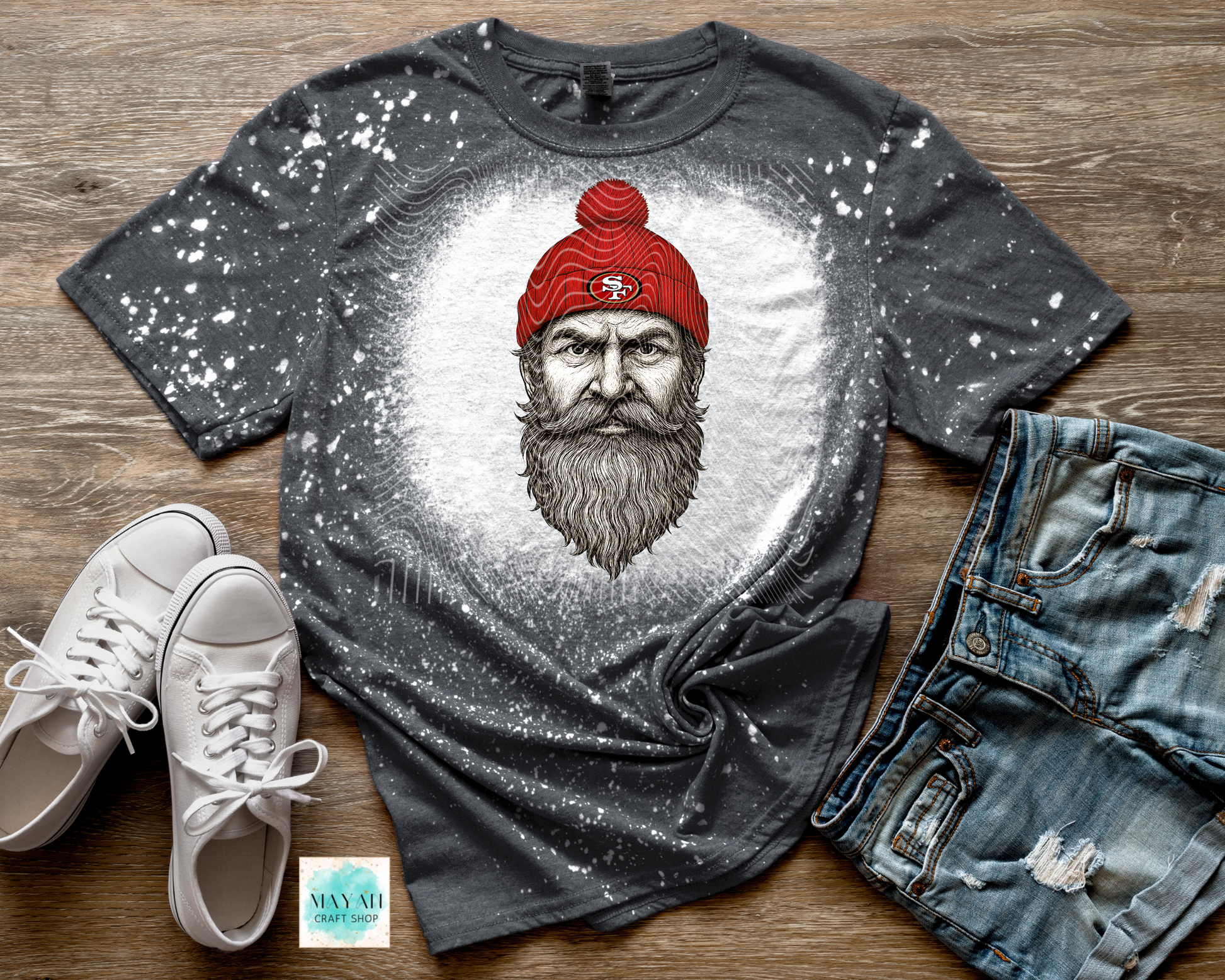 Gray t-shirt with a graphic of a bearded man wearing a red cap, paired with white sneakers and blue jeans on a wooden surface.