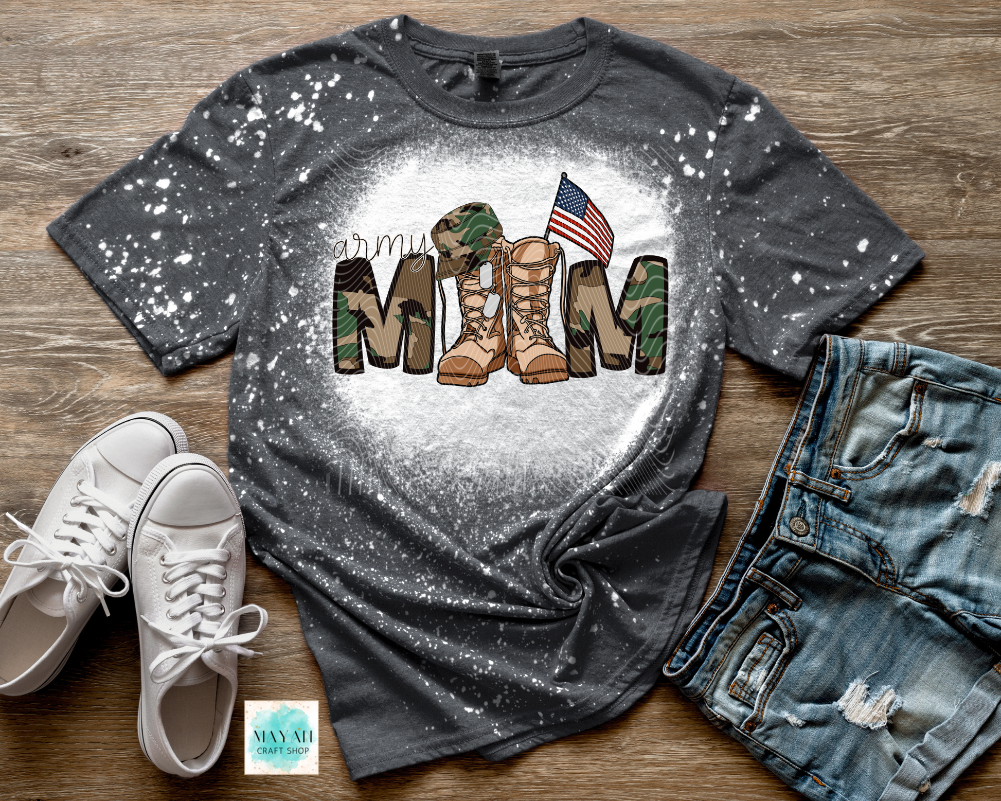 Gray t-shirt with military mom and camouflage boot design on a wooden surface with white sneakers and jeans.