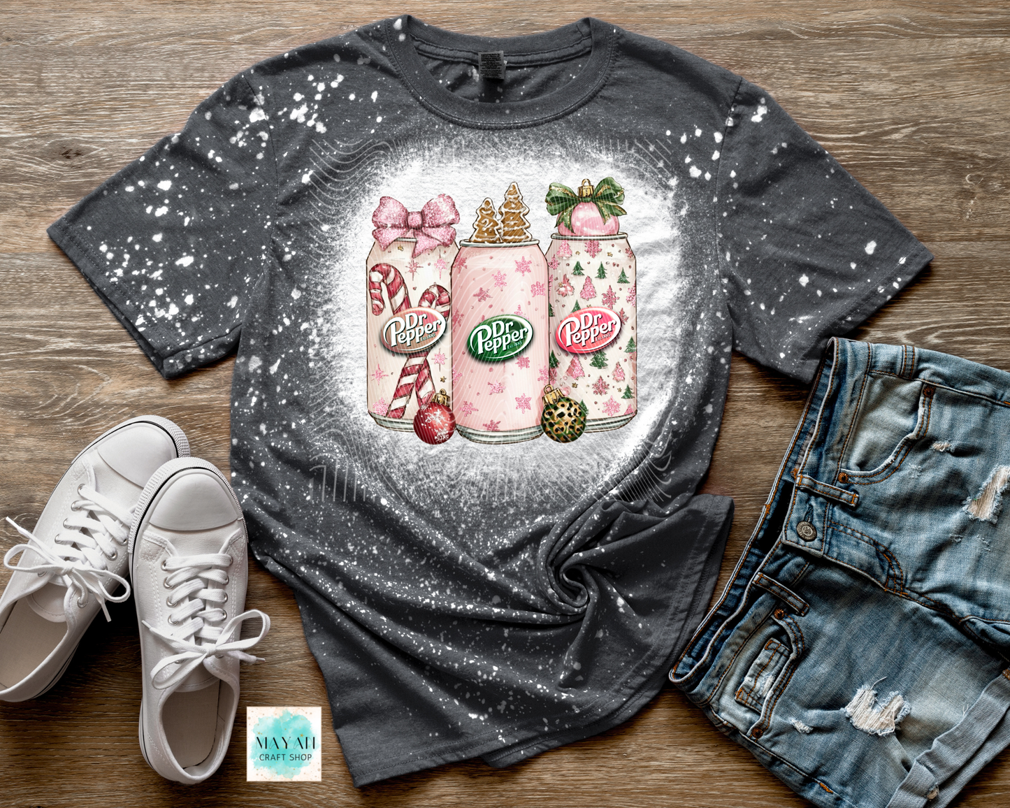 Gray t-shirt with a graphic design of soft drinks bottles, white sneakers, and denim shorts on a wooden surface.