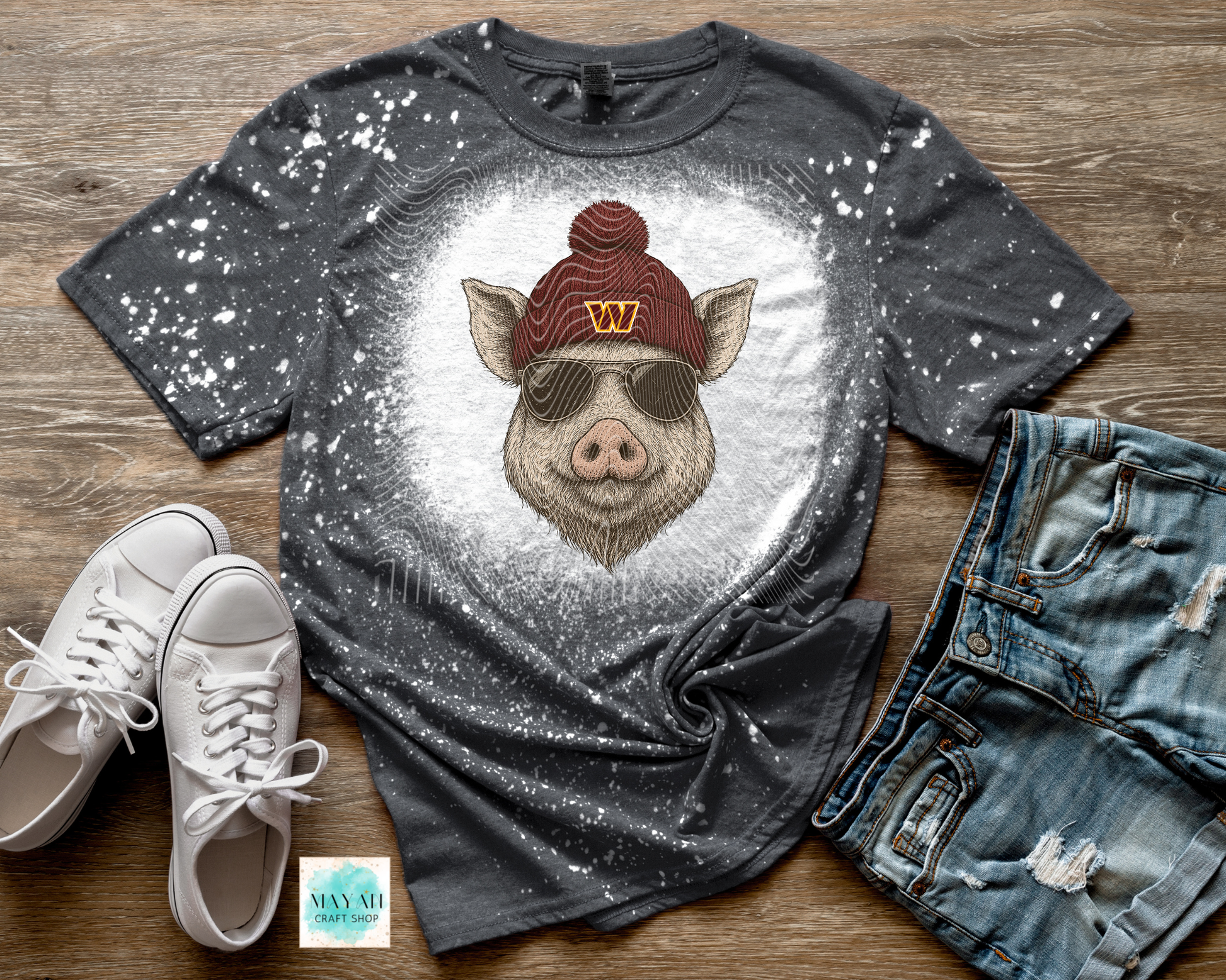 Gray t-shirt with a pig graphic wearing a red beanie, sunglasses, and a 'W' logo, paired with white sneakers and blue jeans on a wooden surface.