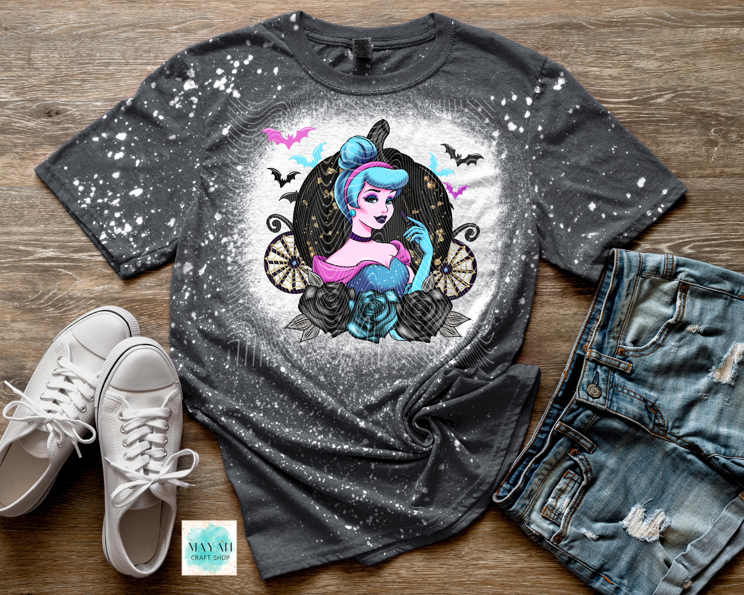 Gray t-shirt with a graphic design of a witch and a carriage, paired with white sneakers and jeans on a wooden surface.