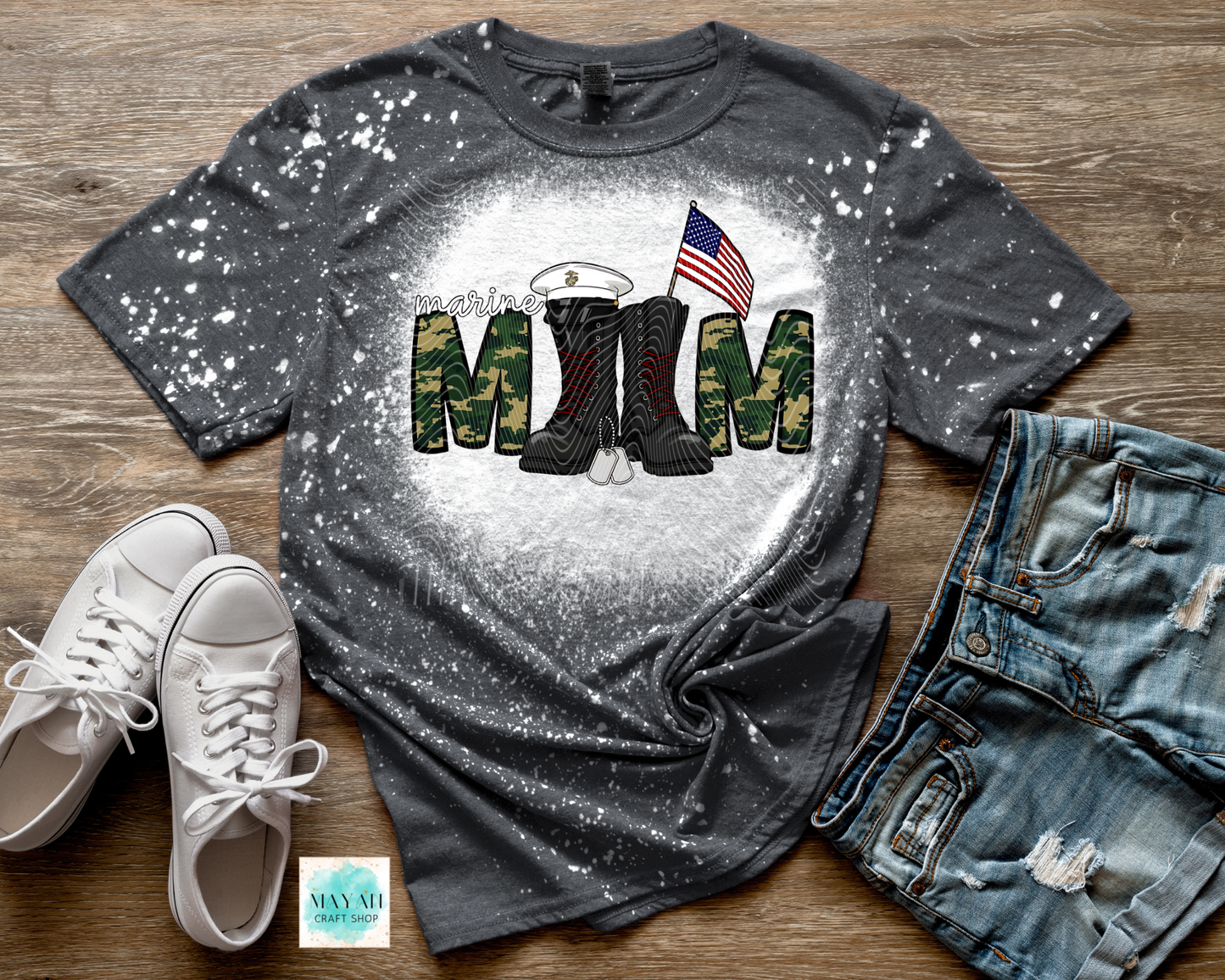 Gray t-shirt with military mom design featuring boots and an American flag, displayed with white sneakers and blue jeans on a wooden surface.