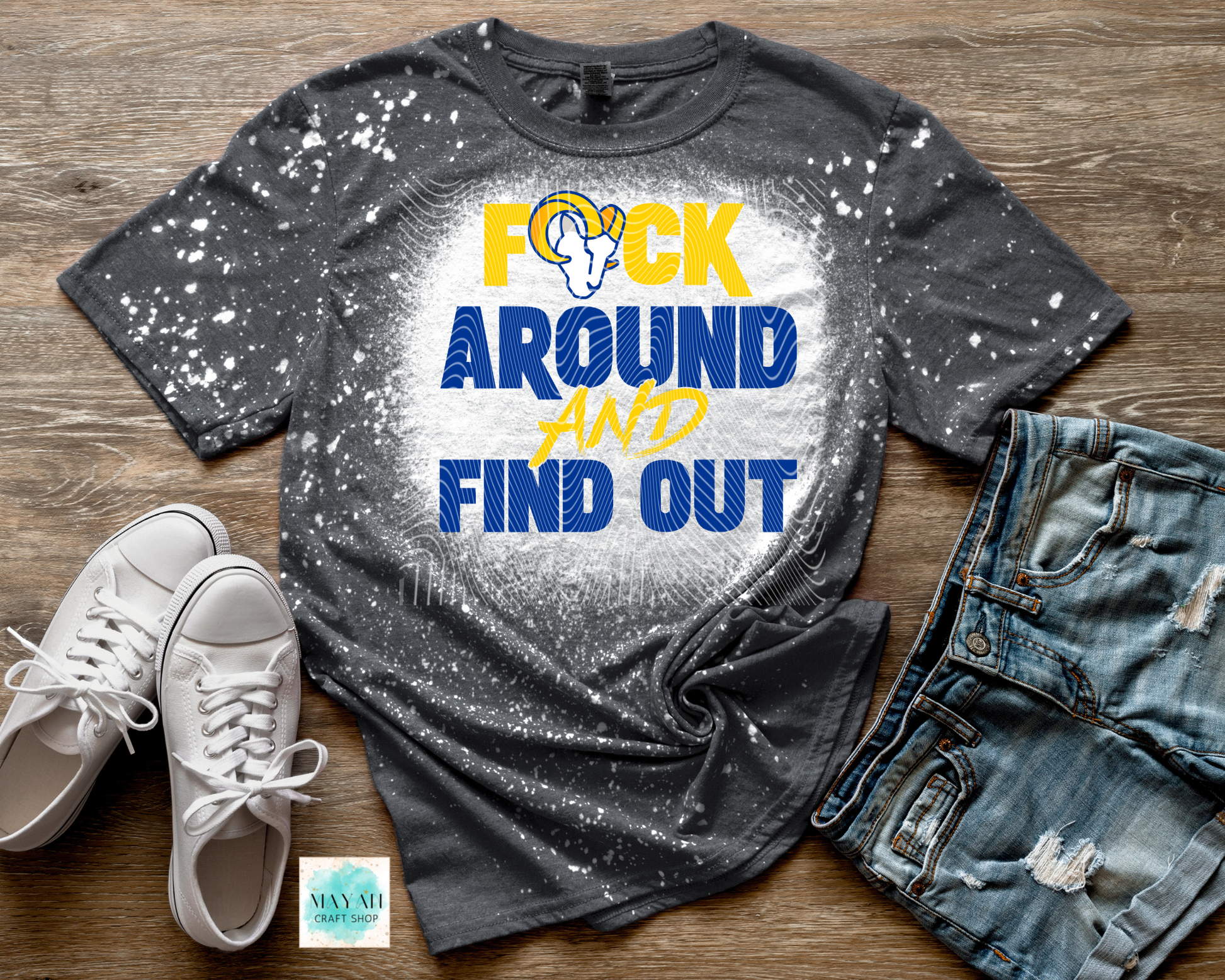 Gray t-shirt with graphic design and text on a wooden surface with shoes and jeans.