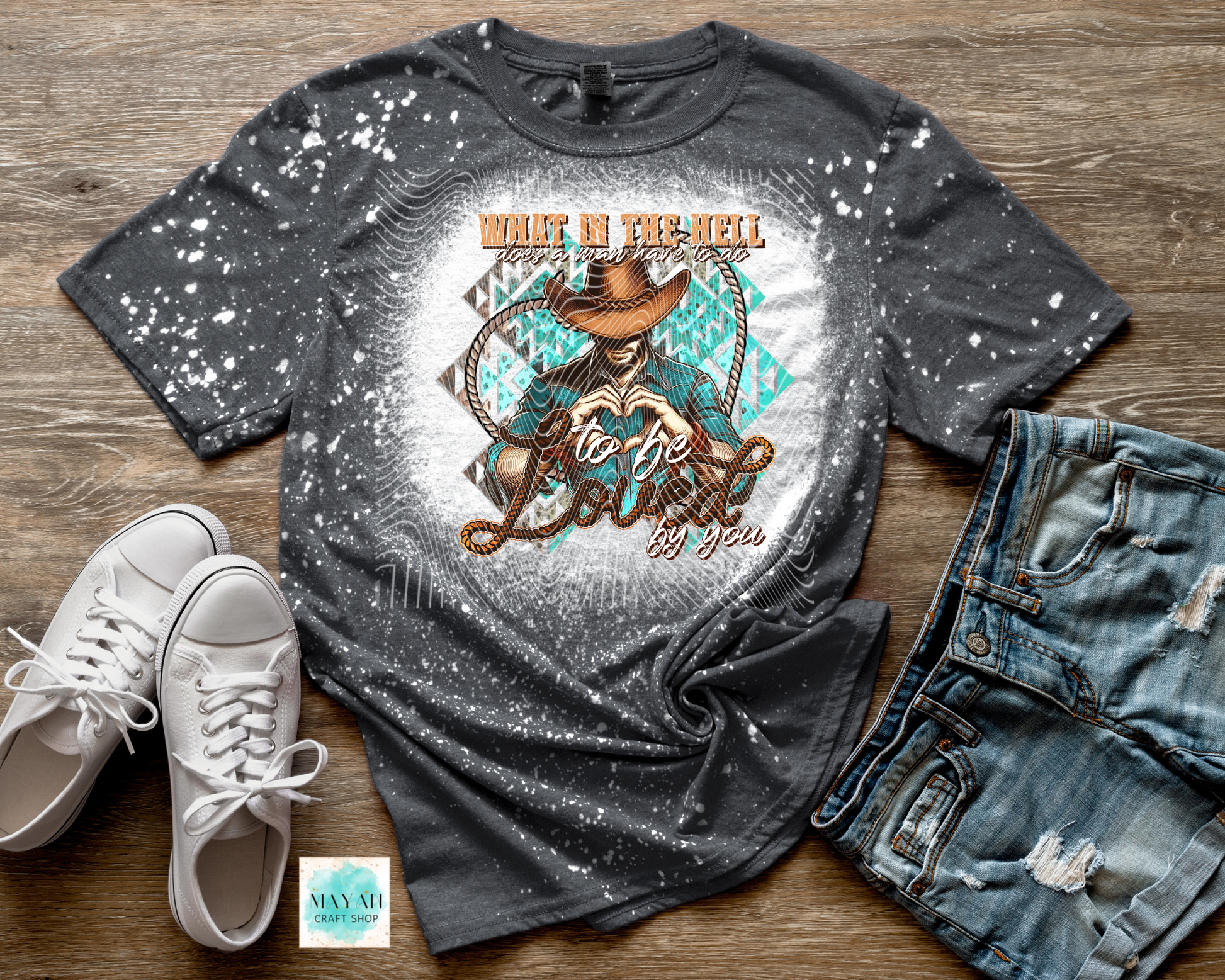 Gray t-shirt with graphic design, white sneakers, and jeans on a wooden surface