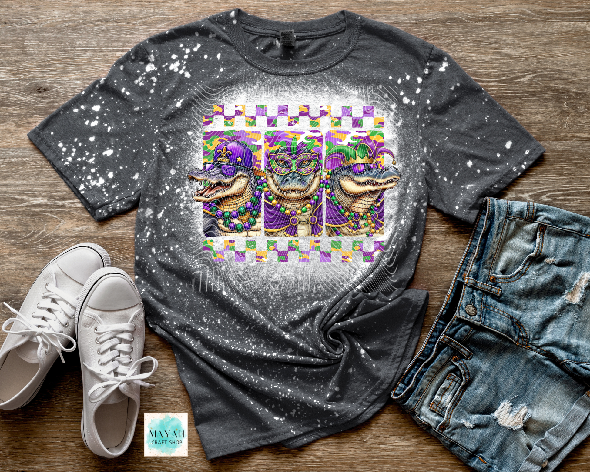 Gray t-shirt with a graphic design of three alligators in Mardi Gras attire on a wooden surface, with white sneakers and jeans.