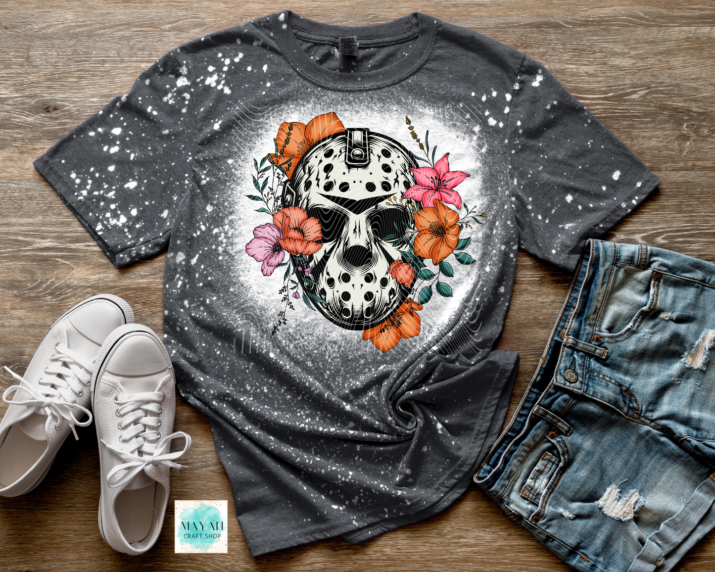 Gray t-shirt with skull and floral design on a wooden surface with sneakers and jeans.