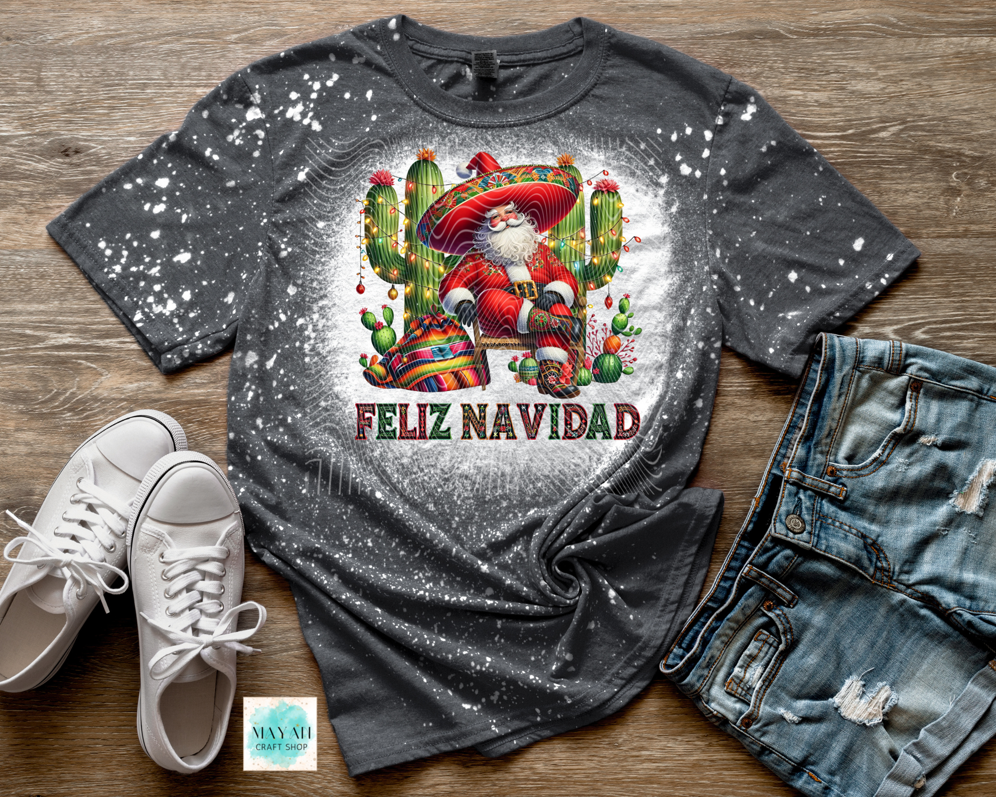 Gray t-shirt with Santa Claus graphic and 'Feliz Navidad' text on a wooden surface with shoes and jeans.