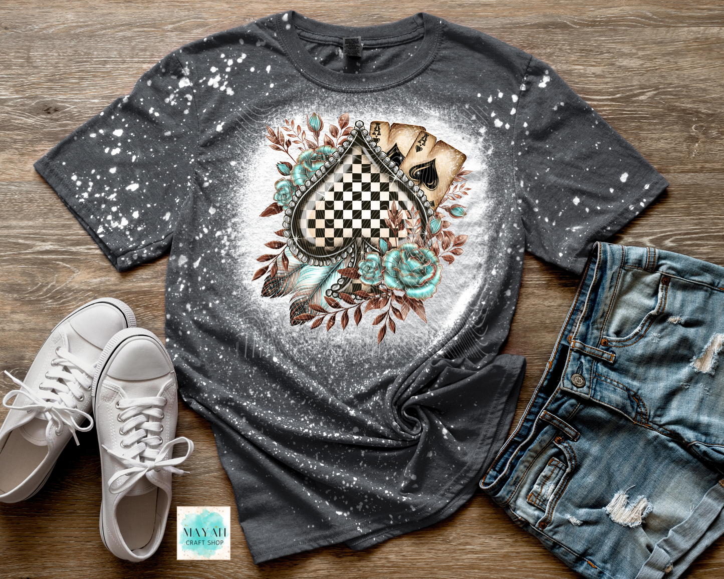 Gray t-shirt with a decorative design on a wooden surface with white sneakers and jeans.