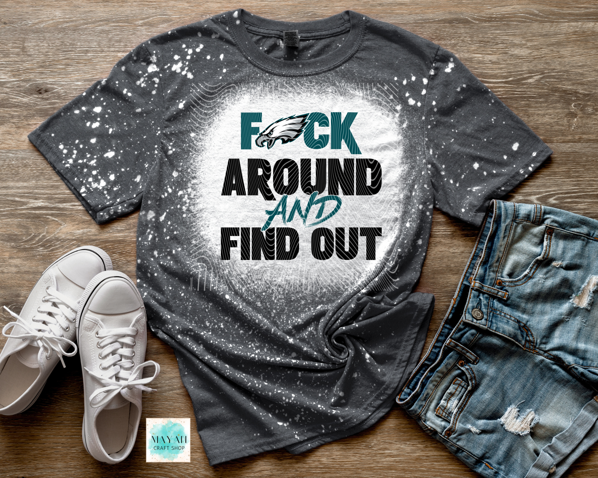 Gray splatter paint t-shirt with text, white sneakers, and jeans on a wooden surface