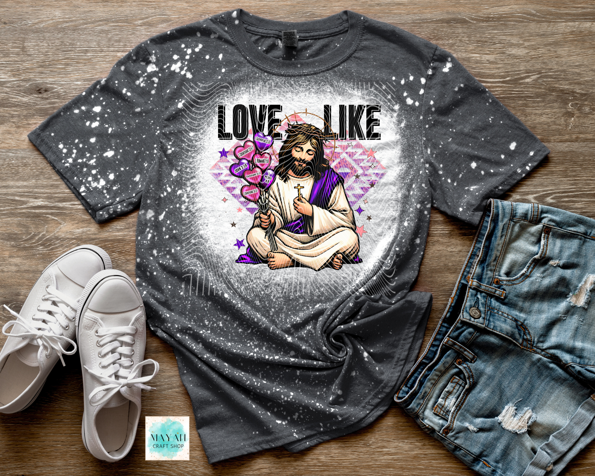 Gray t-shirt with a graphic design of a person holding a heart, surrounded by hearts and the text 'LOVE LIKE', paired with white sneakers and denim shorts on a wooden surface.
