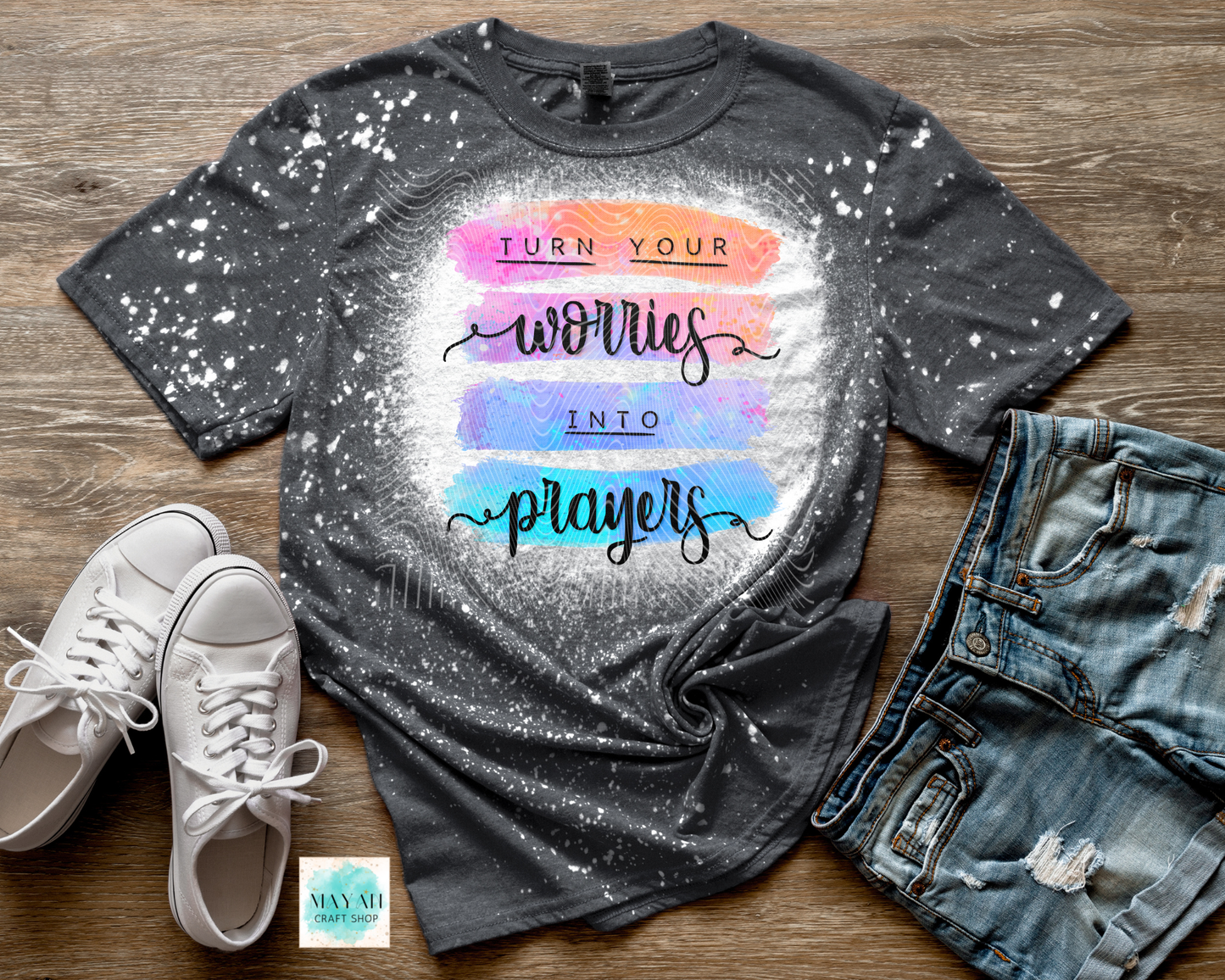 Gray bleached t-shirt with colorful text, white sneakers, and denim shorts on a wooden surface.