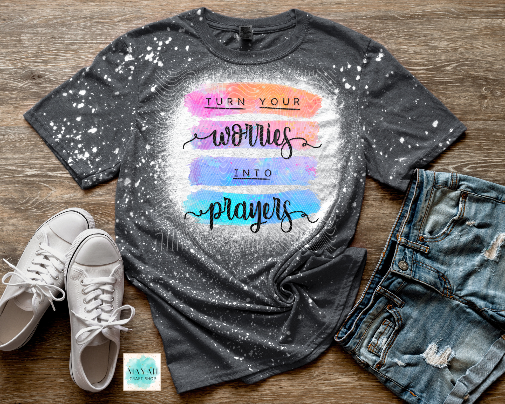 Gray bleached t-shirt with colorful text, white sneakers, and denim shorts on a wooden surface.
