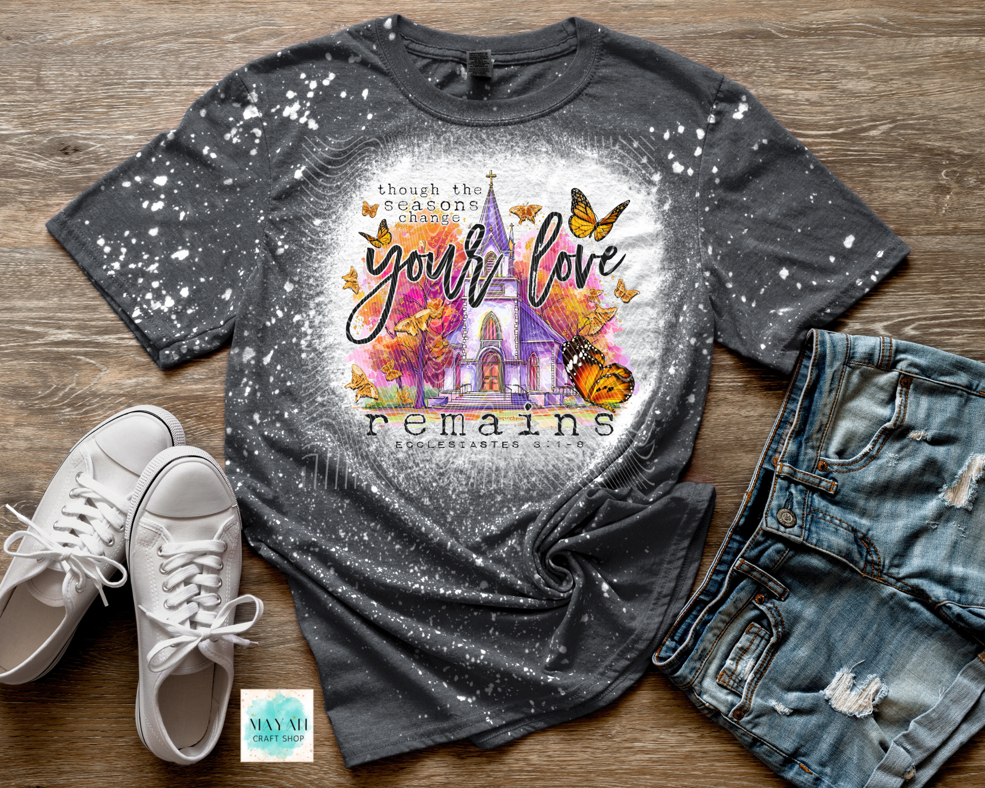 Gray t-shirt with colorful design and text on a wooden surface with shoes and jeans.