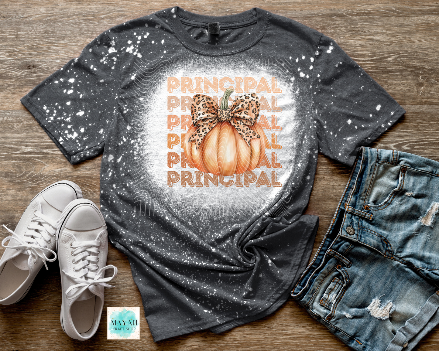 Gray t-shirt with 'Principal' and pumpkin design, paired with white sneakers and jeans on a wooden surface.