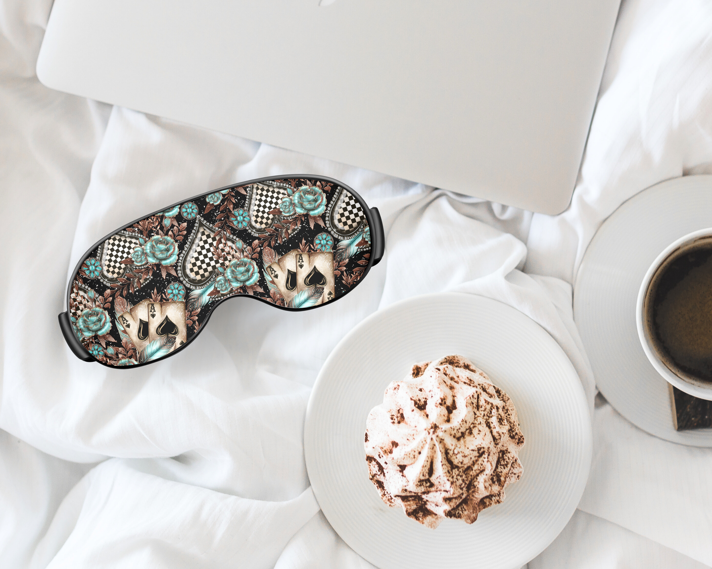 Sleep mask with cat design on a white surface with a cup of coffee and dessert.