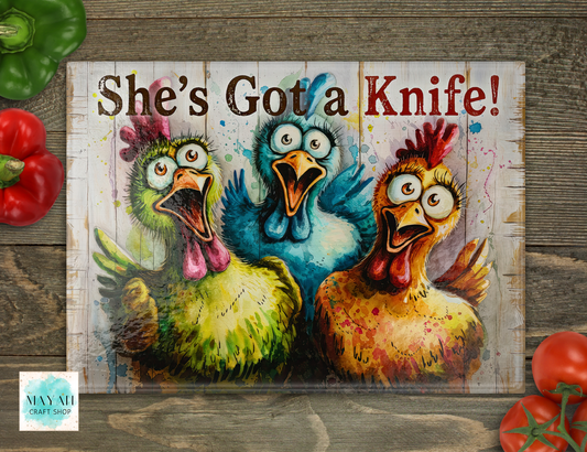 Decorative sign with cartoon chickens and text 'She's Got a Knife!' on a wooden background.