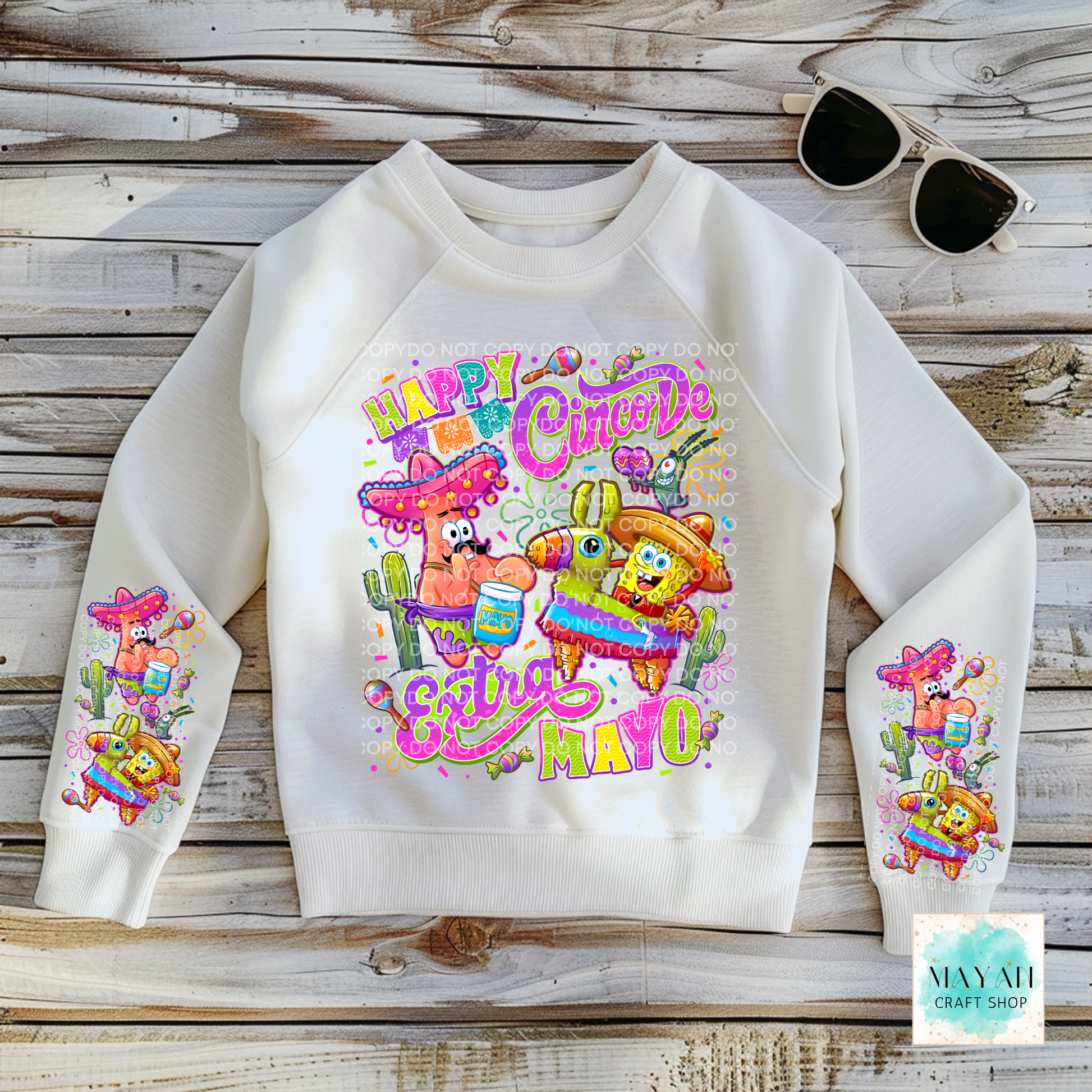 White sweatshirt with colorful graphic design on a wooden surface, featuring sunglasses and a brand logo.