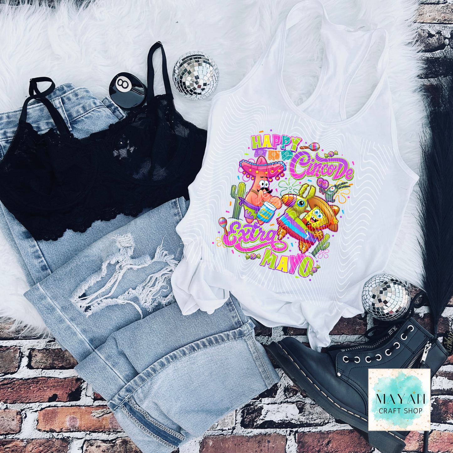 White tank top with colorful 'Happy Cinco de Mayo' design, black bralette, denim shorts, and black high-heeled shoes on a brick surface.