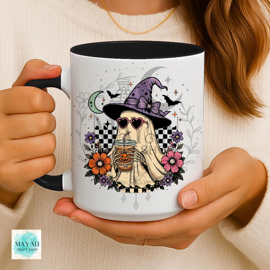 Person holding a mug with a ghost in a witch hat design, featuring flowers and a moon.