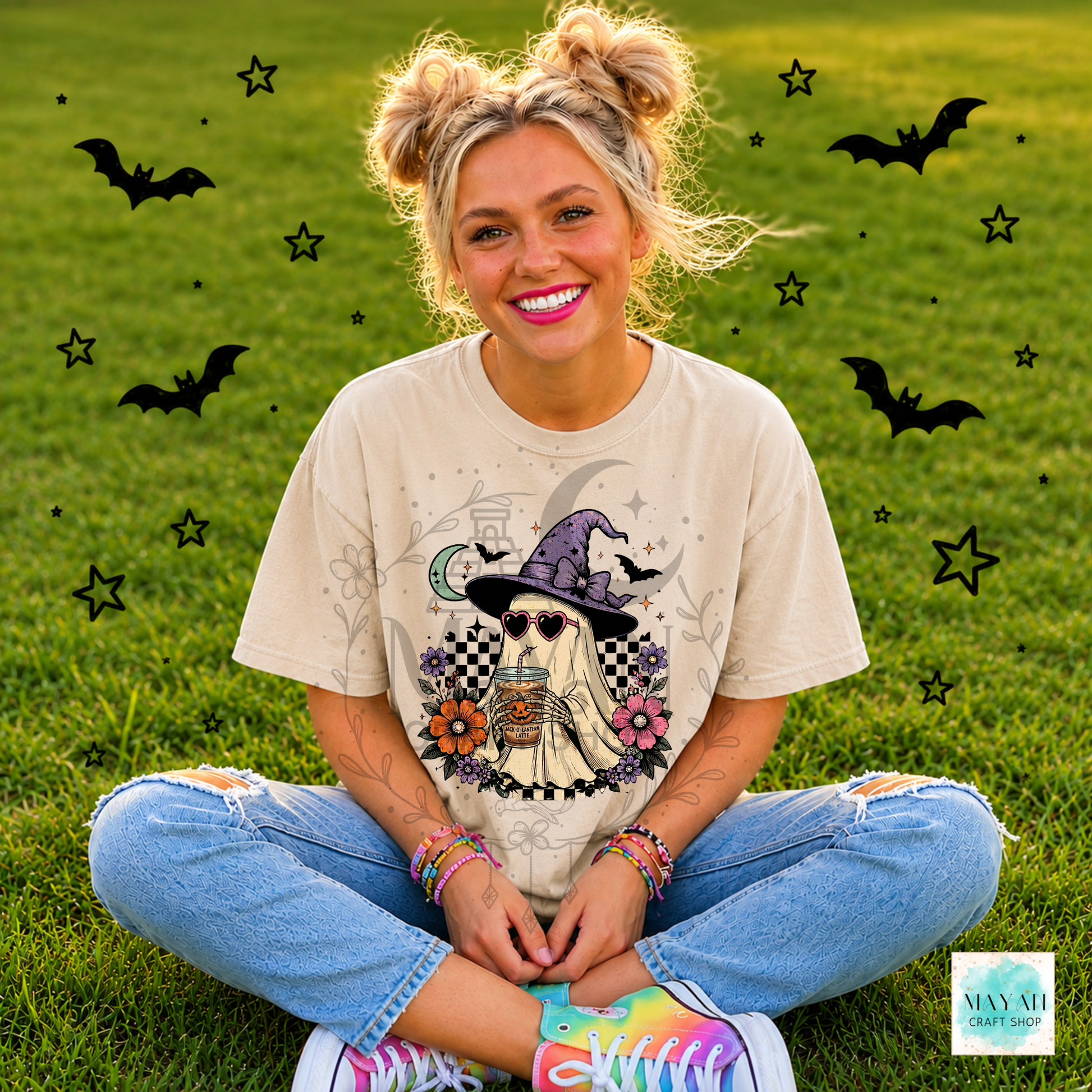 Person wearing a Halloween-themed t-shirt with a ghost in a witch hat design, sitting on grass with decorative elements.