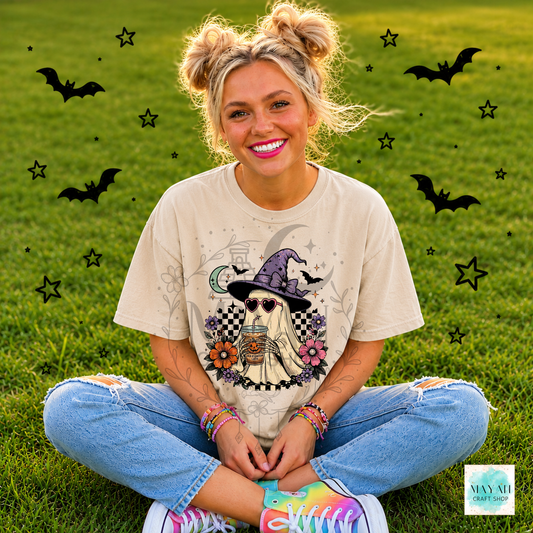 Person wearing a Halloween-themed t-shirt with a ghost in a witch hat design, sitting on grass with decorative elements.