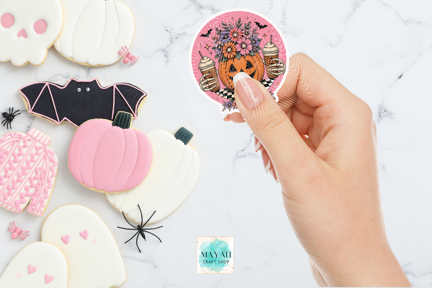 Decorative Halloween cookies with a hand holding a circular sticker with floral and pumpkin design.