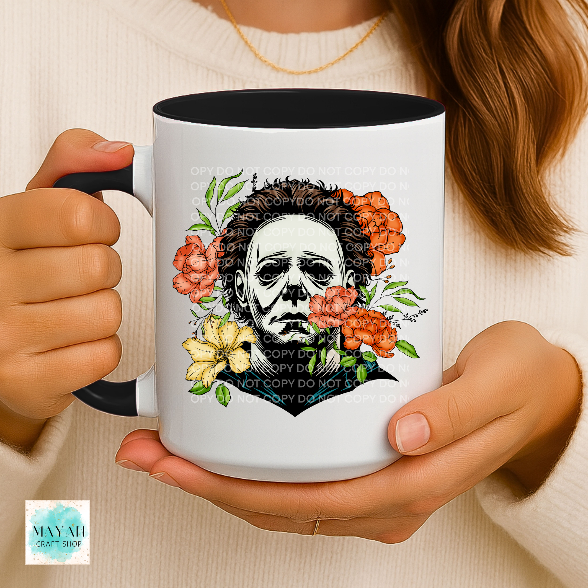 Person holding a mug with a design of a face surrounded by flowers, wearing a white sweater.
