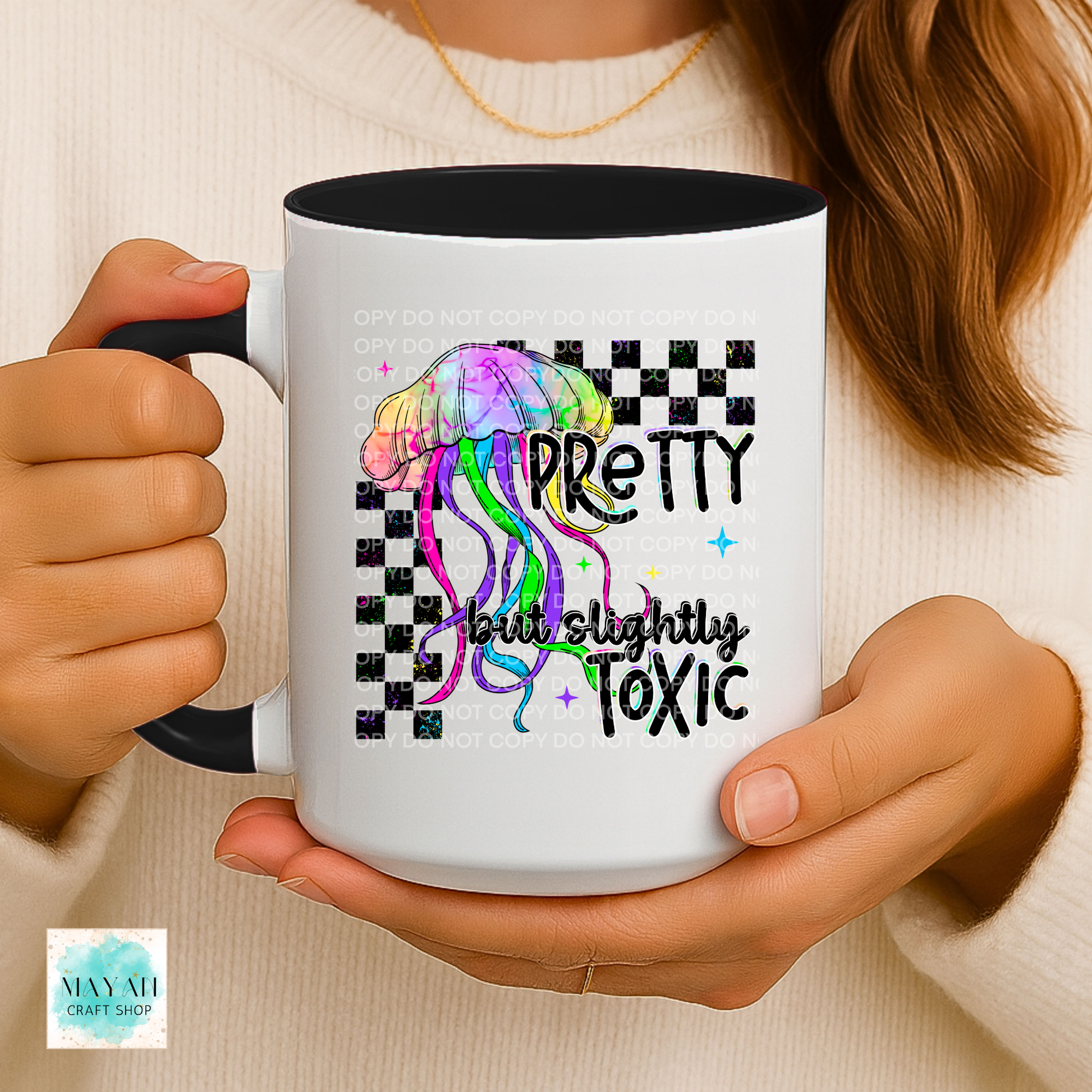 Person holding a mug with a colorful jellyfish design and text 'Pretty but slightly toxic' on a checkered background.