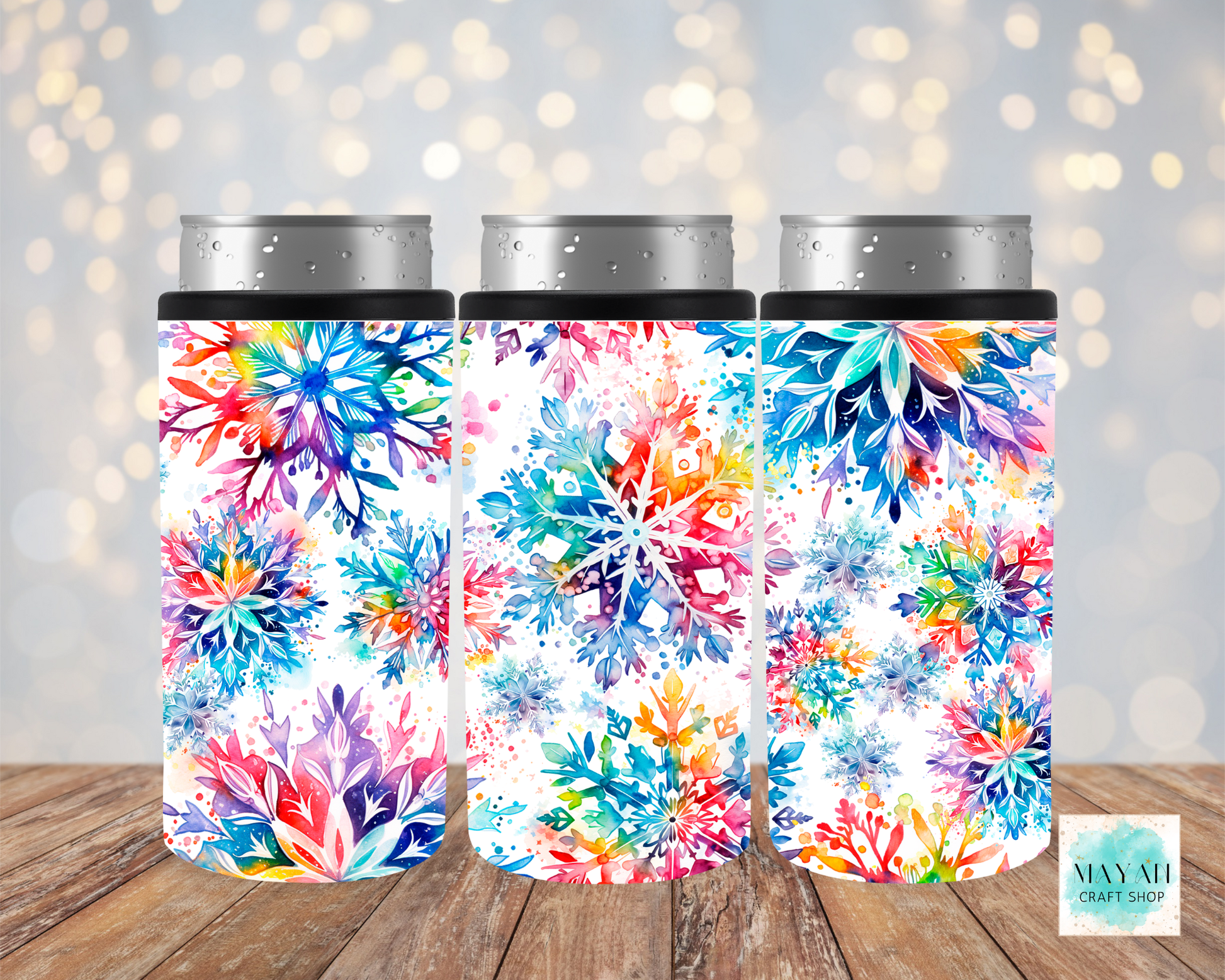 Three colorful floral can coolers on a wooden surface with a bokeh background.