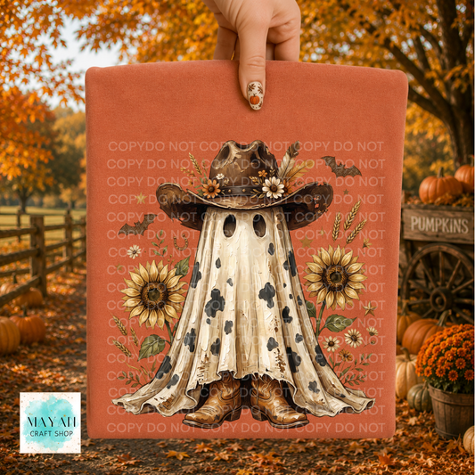 A hand holds a shirt with a fall-themed ghost in a cowboy hat design, set against an autumn outdoor background with pumpkins, fall leaves, and a wooden fence. The sign has a terracotta background with a central illustration of a ghostly figure in a cowboy outfit, surrounded by sunflowers and small wildflowers.