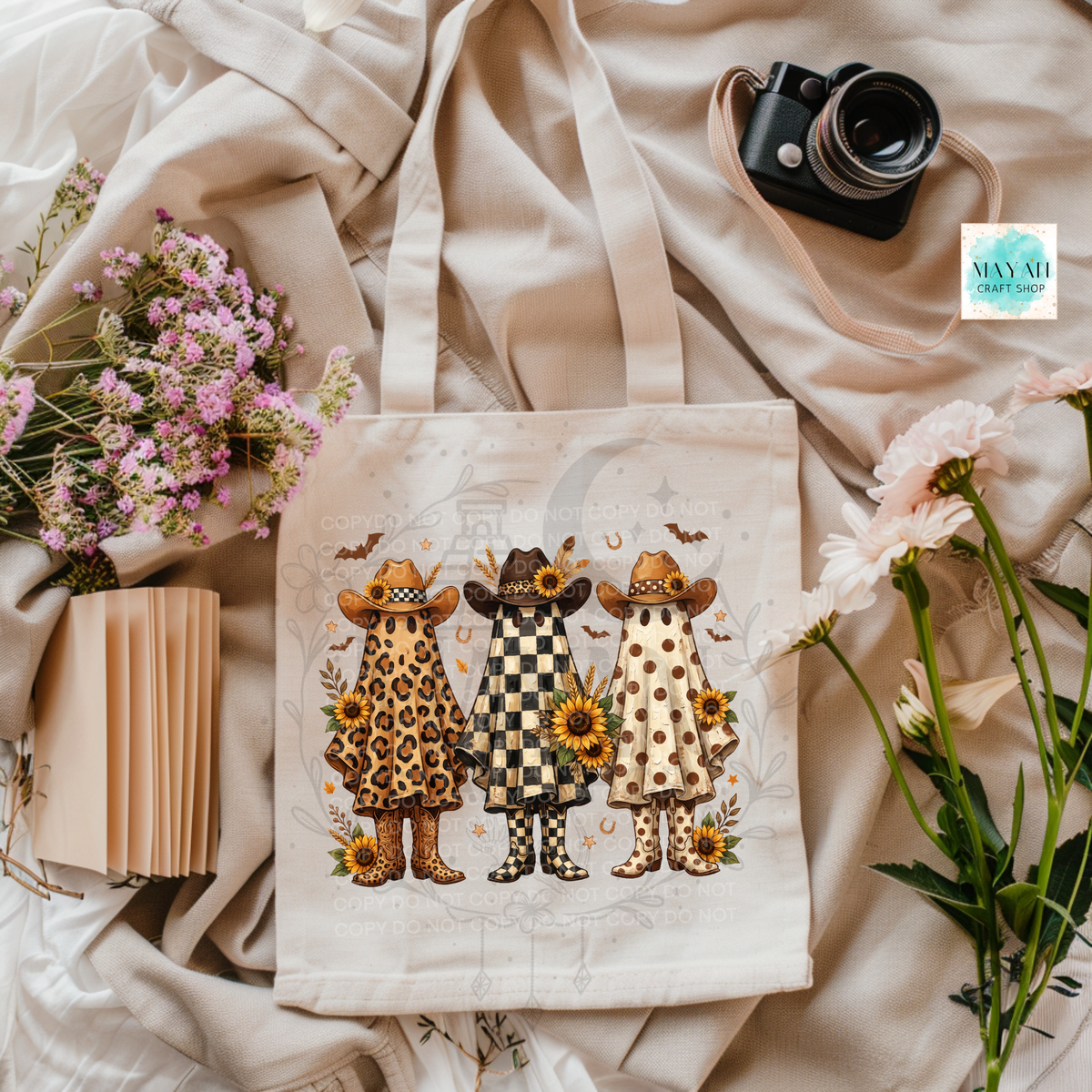 A cream canvas tote bag with a printed illustration of three cartoon children in animal-print and checkered outfits, styled on beige fabric with flowers, a camera, and a small book. 