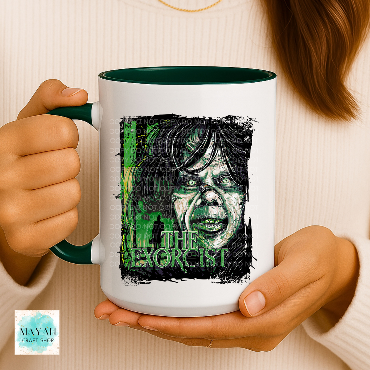 A person holds a white ceramic mug with a dark green handle and interior. The mug features a graphic print of a zombie face with a text in green.