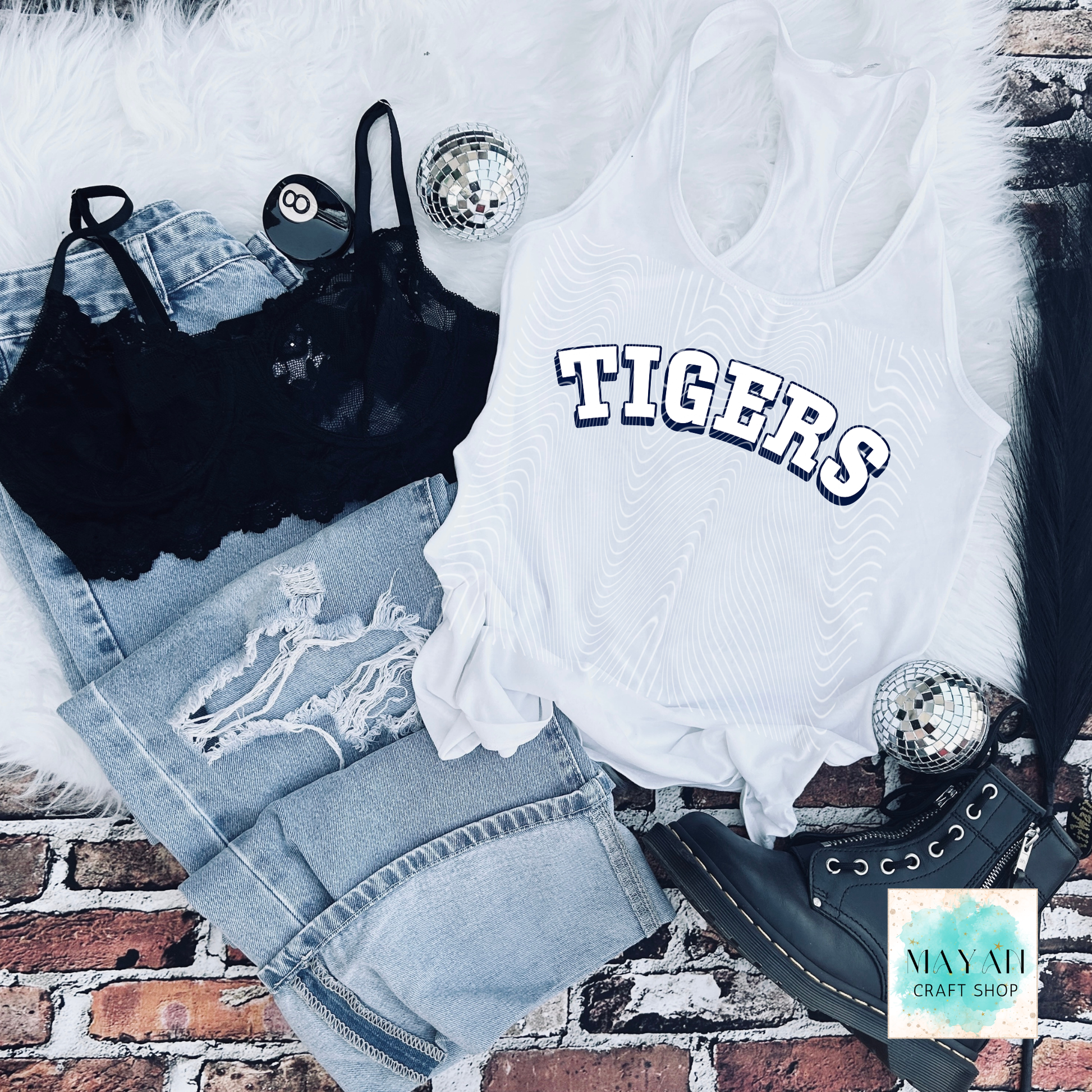 White tank top with baseball logo text, black bralette, denim shorts, and black high-heeled shoes on a brick surface.