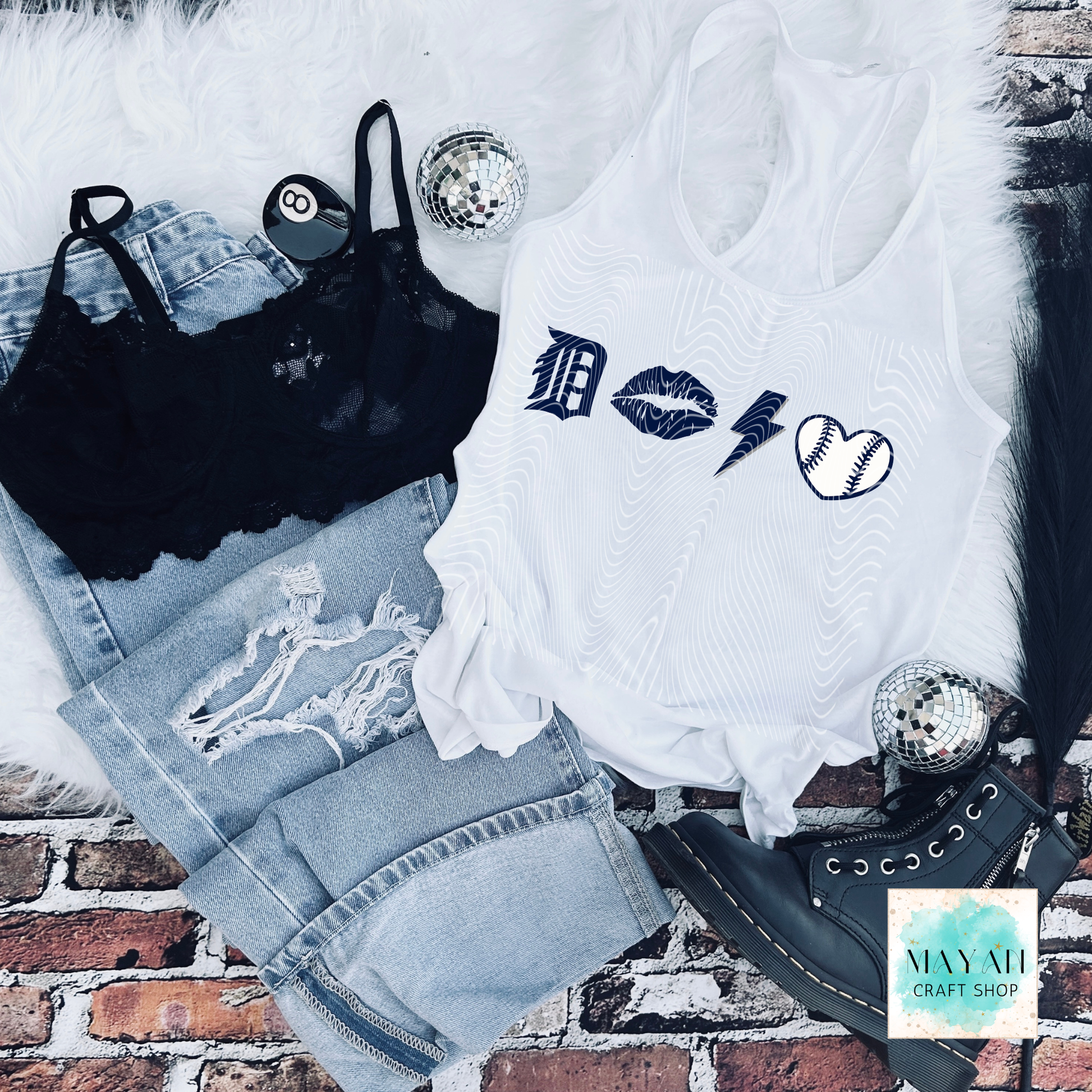 White tank top with graphic designs on a brick surface with denim shorts and black lace top.