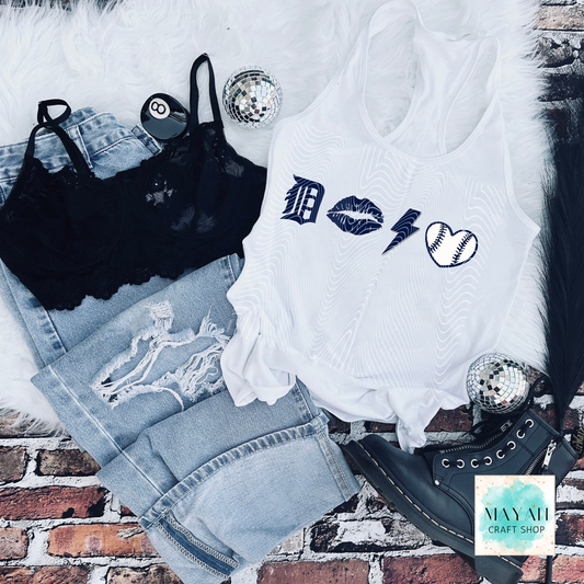 White tank top with graphic designs on a brick surface with denim shorts and black lace top.